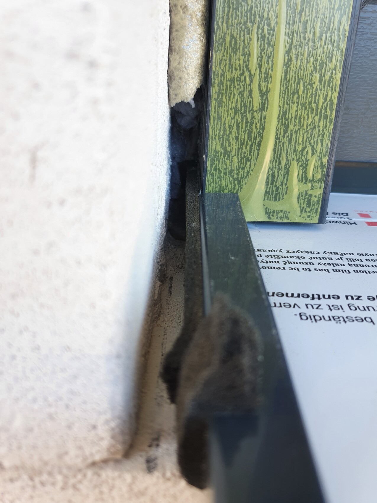 Nahaufnahme einer Fuge zwischen weißer Wand und grünem Holzrahmen, Staub sichtbar.