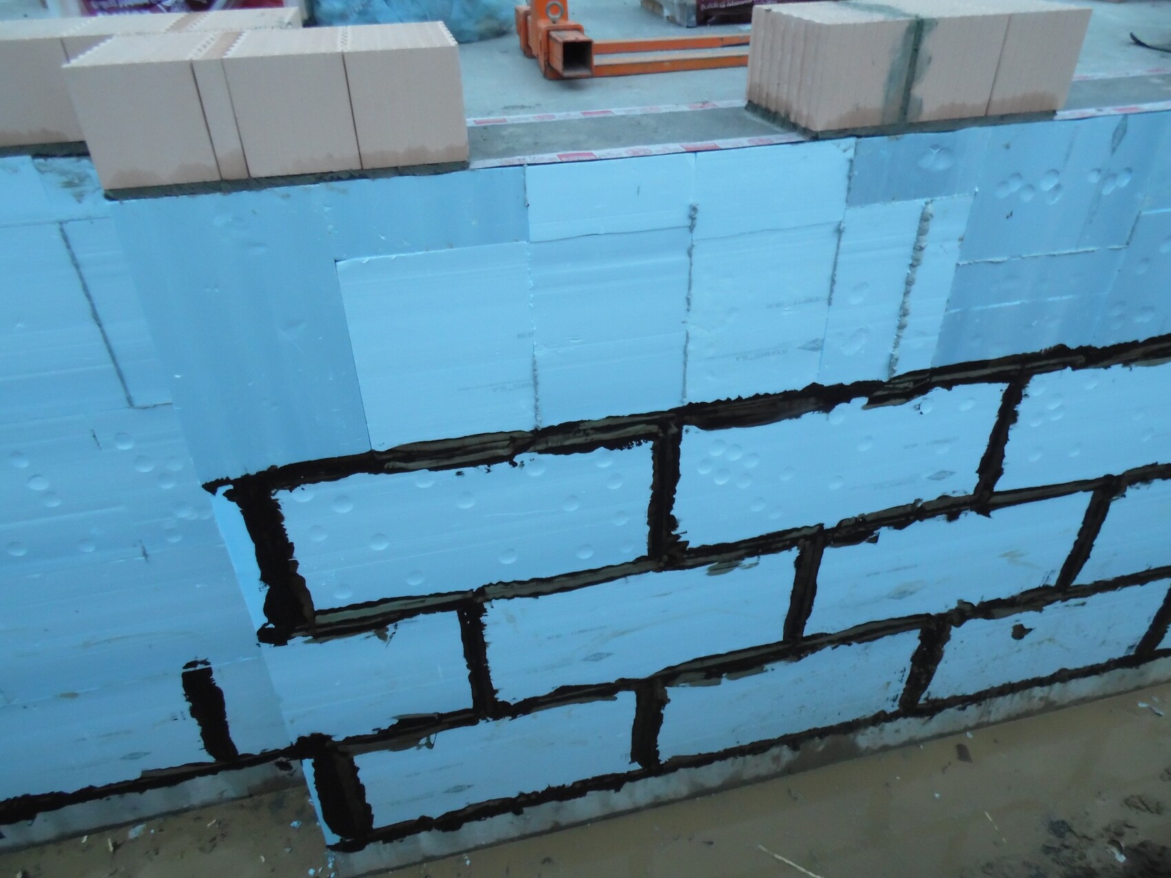 Blaue Dämmplatten aus Polystyrol an einer Fundamentwand auf einer Baustelle, schwarze Abdichtung sichtbar