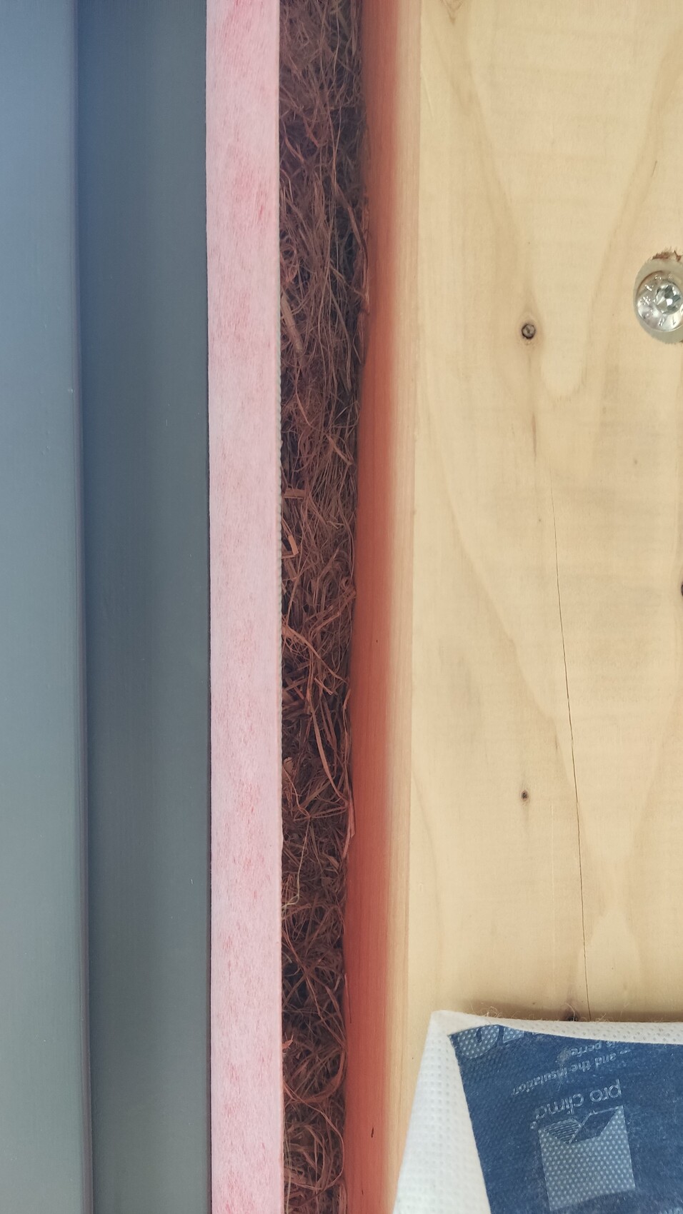 Türrahmenbereich: Metallrahmen links, rosa Dämmstoffstreifen, braunes Fasermaterial, Holzwand rechts.