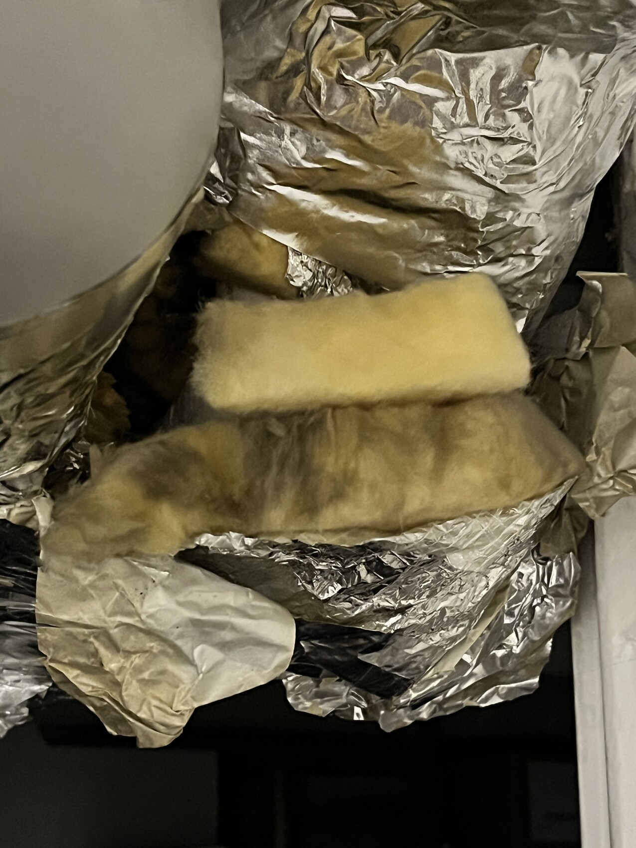 Lüftungsschacht mit zerknitterter Aluminiumfolie und gelber Isolierwatte.
