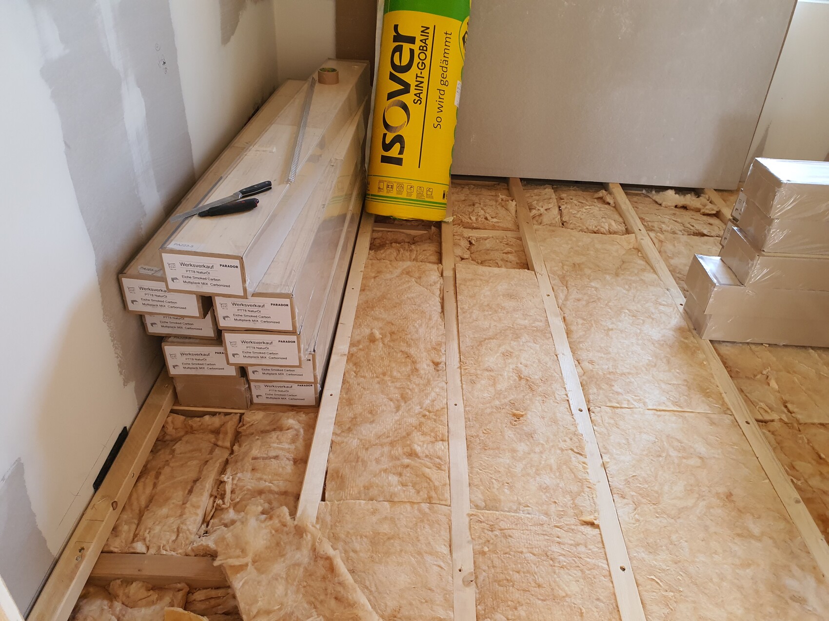 Bauunterbau: freiliegende Holzbalken mit Dämmung, Kartons und Cuttermesser auf einer Baustelle.