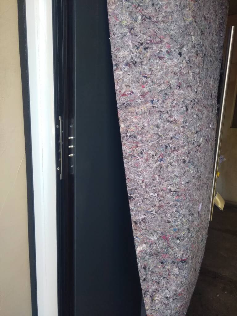 Türrahmen links, daneben eine große, bunte, aufrecht stehende Teppichreste-Matte.
