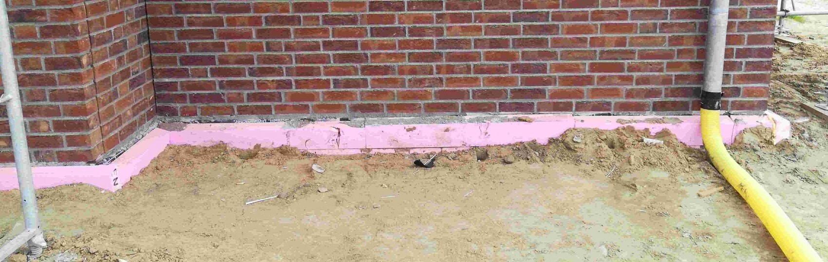 Unteres Mauerwerk eines Neubaus mit pinker Dämmung am Fundament und gelbem Drainageschlauch