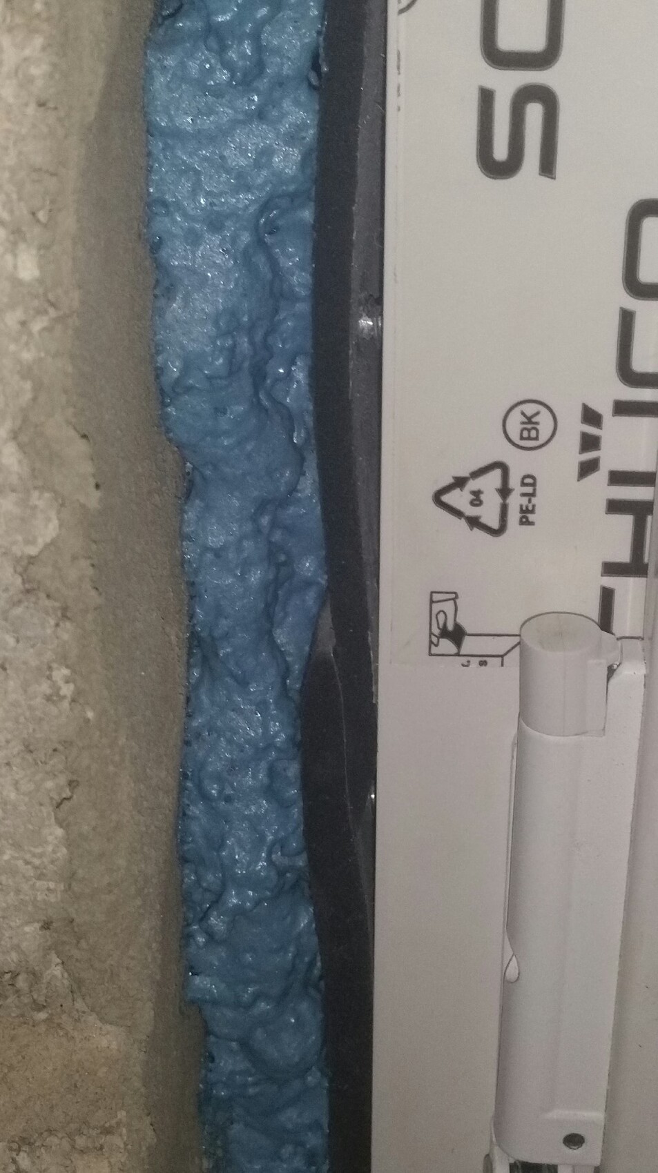 Blaue Daemmungsschaum in Wandöffnung neben Fensterrahmen waehrend Bauarbeiten