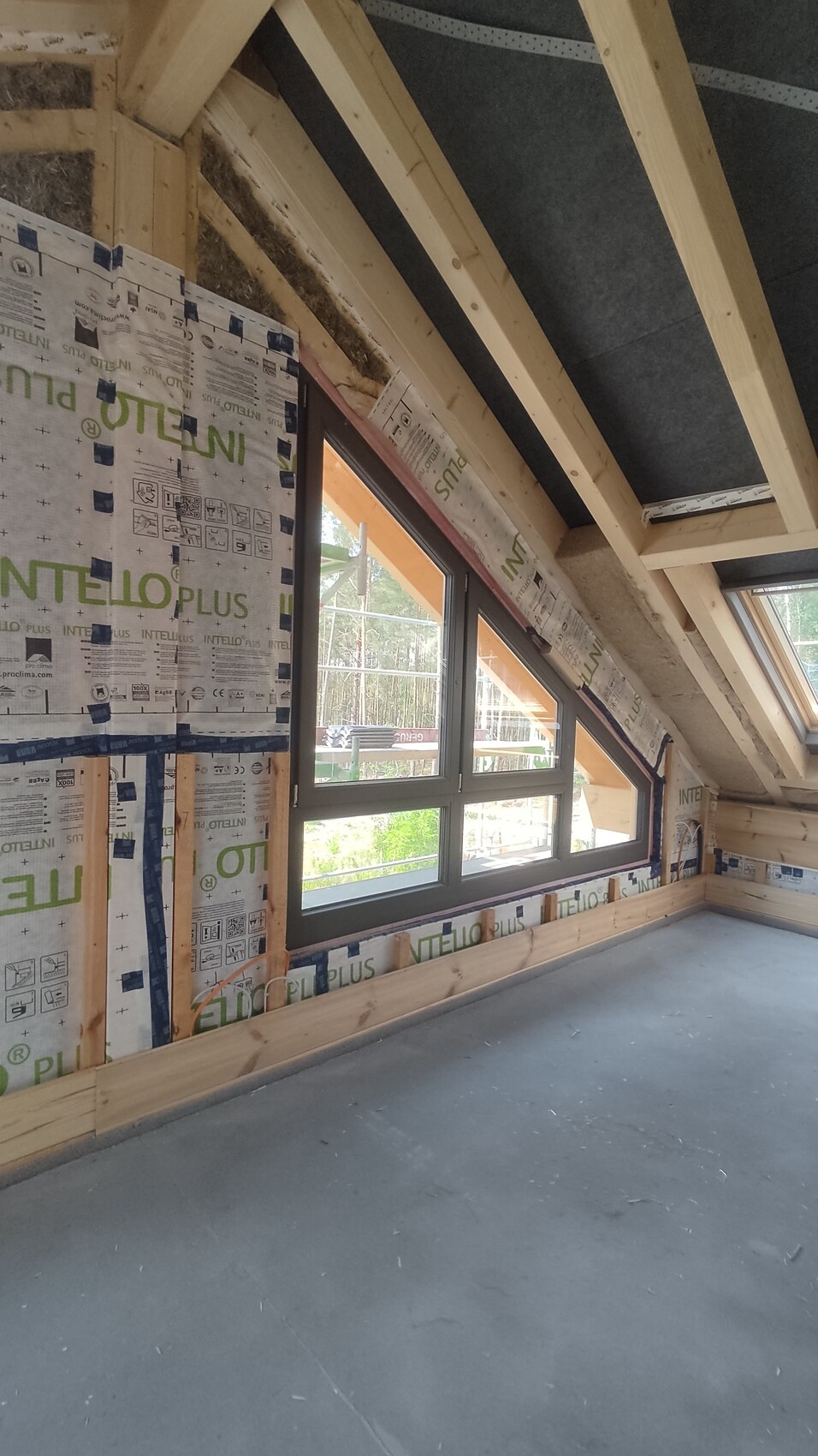 Dachgeschoss-Rohbau mit Holzrahmen, Fenster, INTELLO-PLUS-Dämmung, Blick ins Grüne.