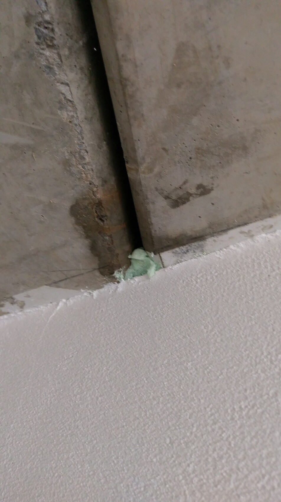 Innenwand-Ecke mit Beton, Rostspuren und gruenem Dämmstoffrest