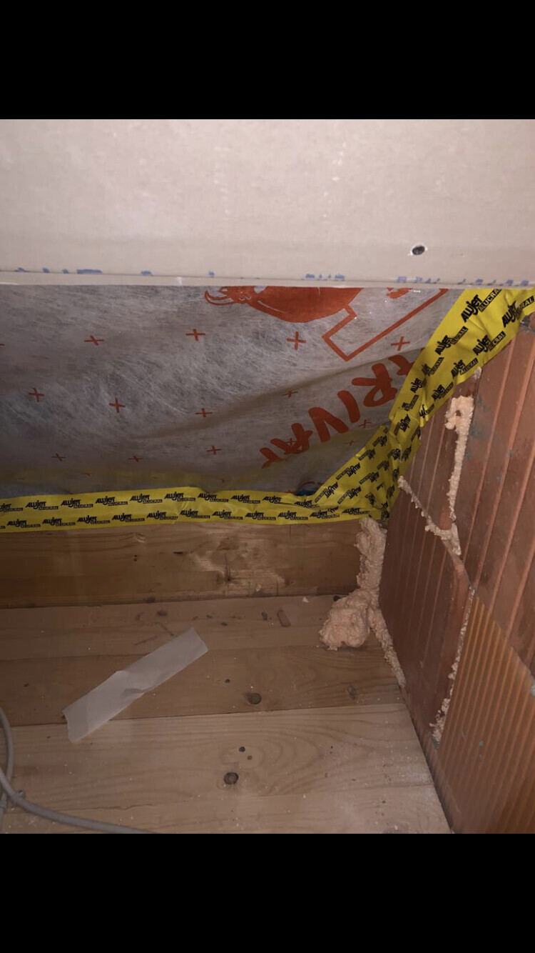 Dachboden-Ecke mit Dämmfolie, Gelbes Klebeband, Holzbodenplatten und Putzreste.