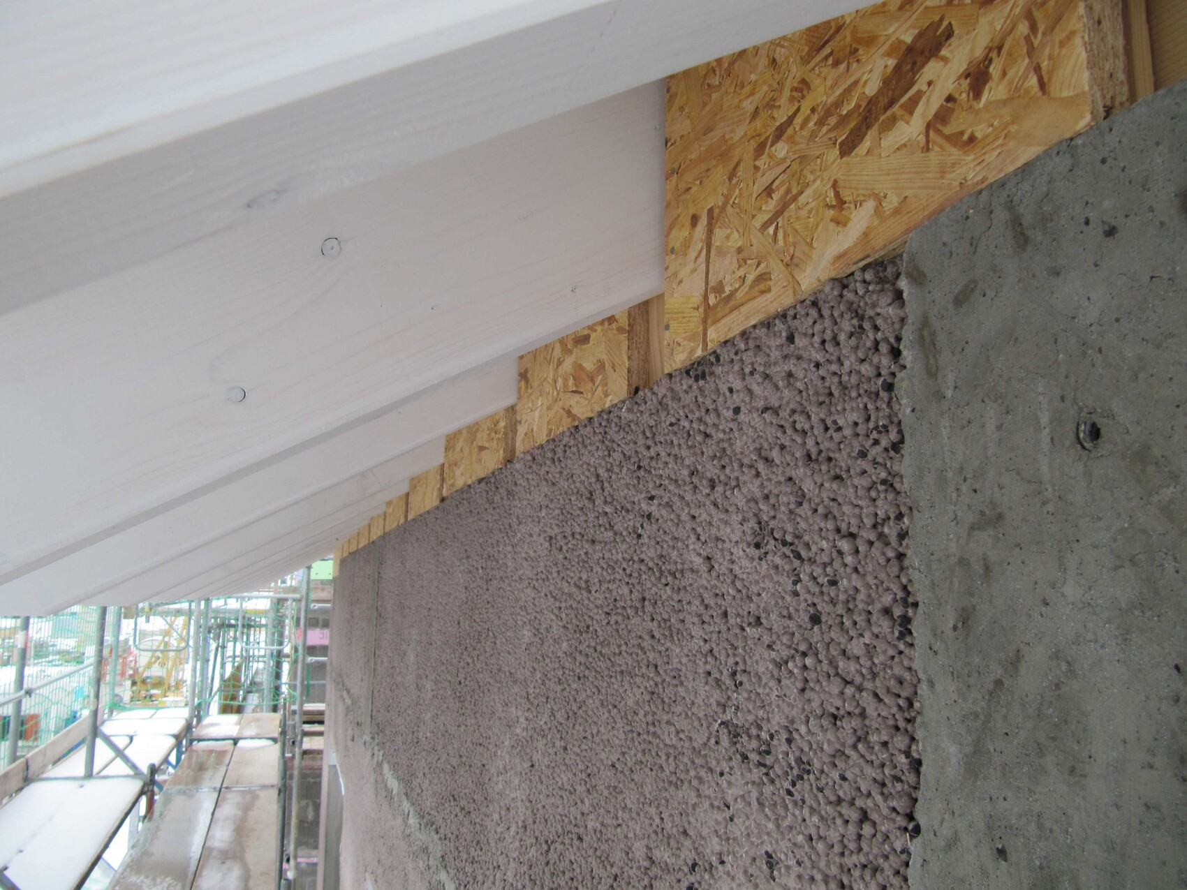 Baustellwand mit Holzverkleidung, OSB-Platte und Perlen-Dämmung im Rohbau, Gerüst sichtbar