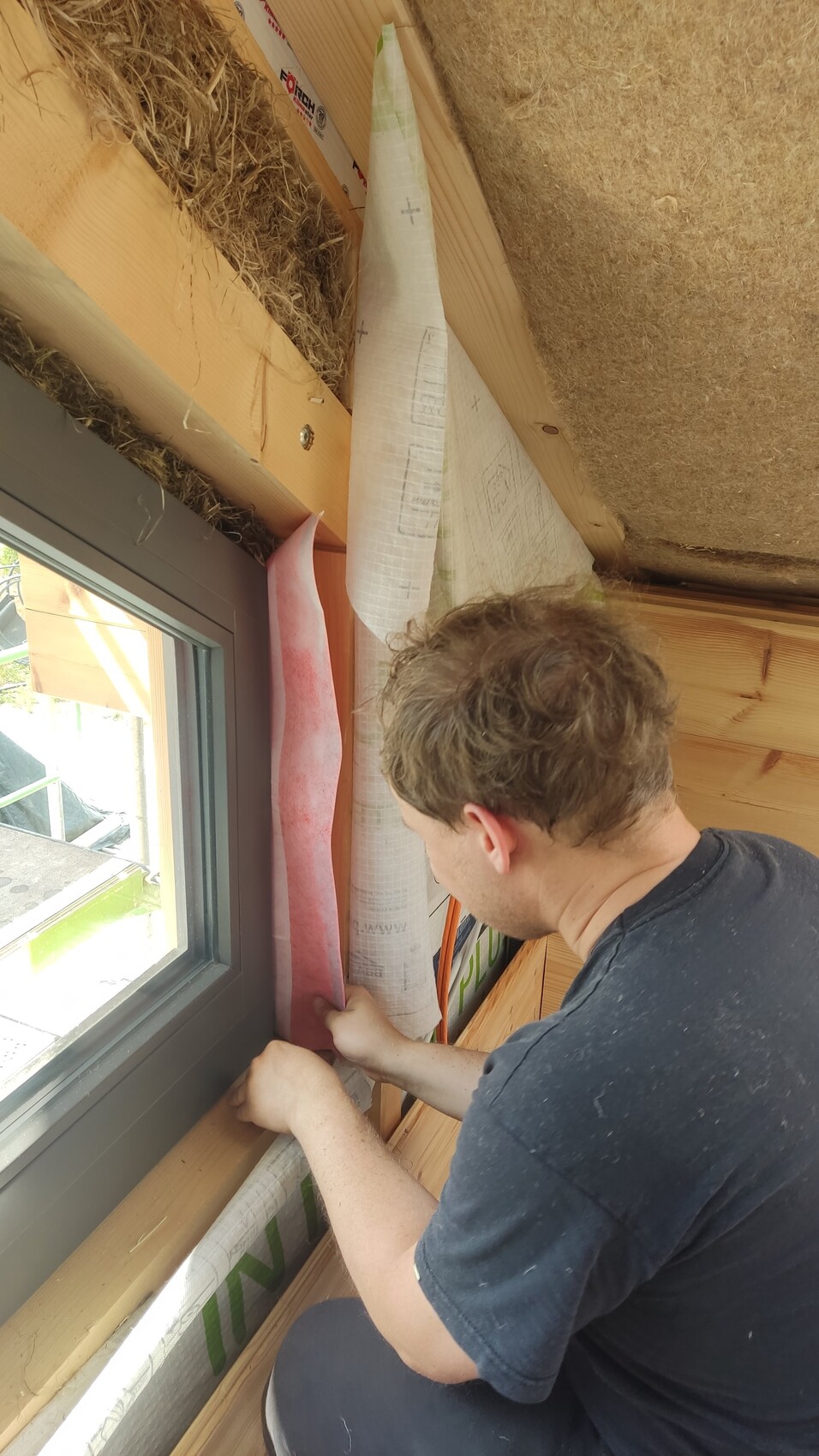 Mann montiert rosa Dämmstoffstreifen im Holzrahmen um ein Fenster.