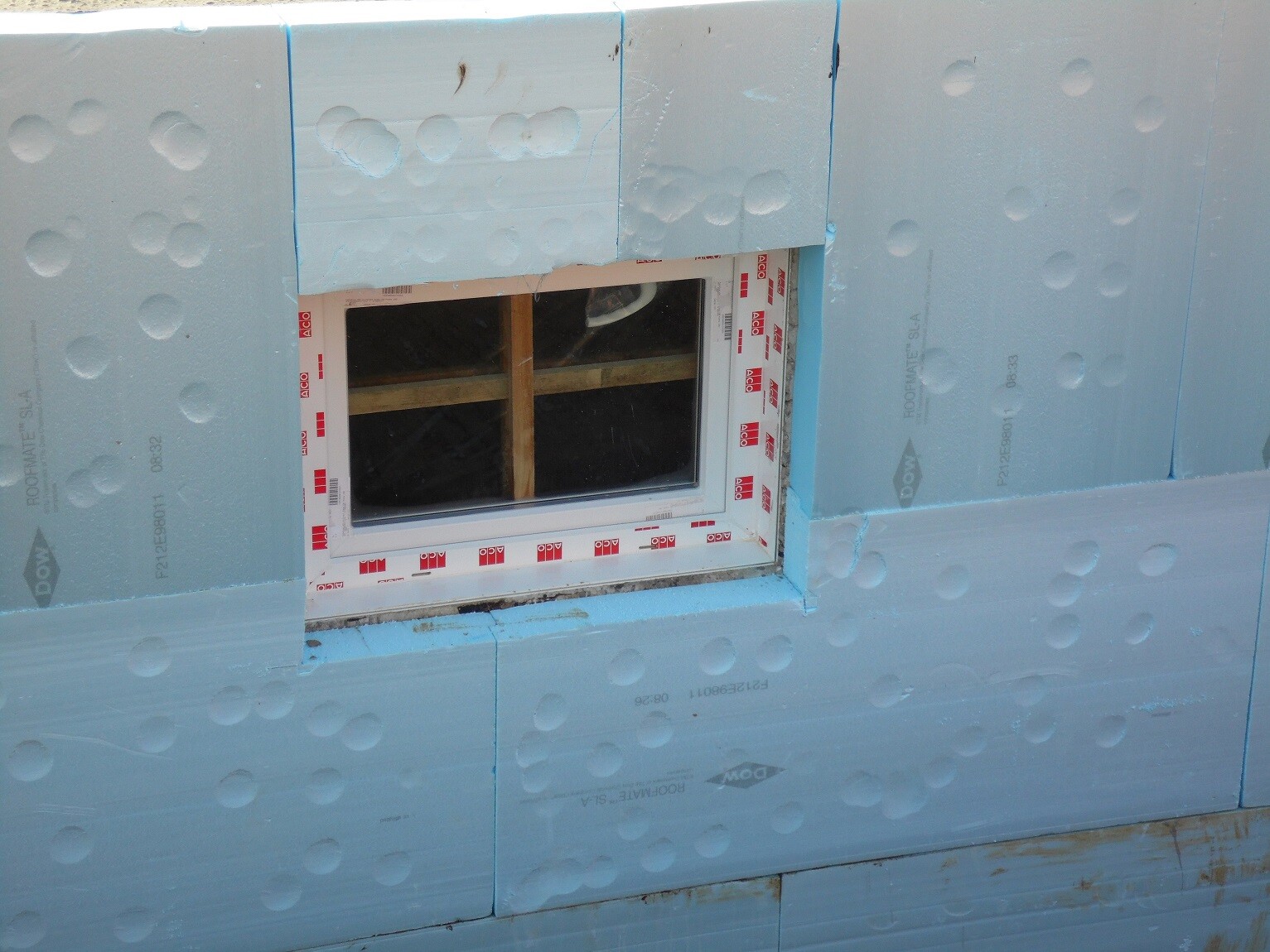 Außenwand mit blauer Dämmplatte und Fensterrahmen im Bau