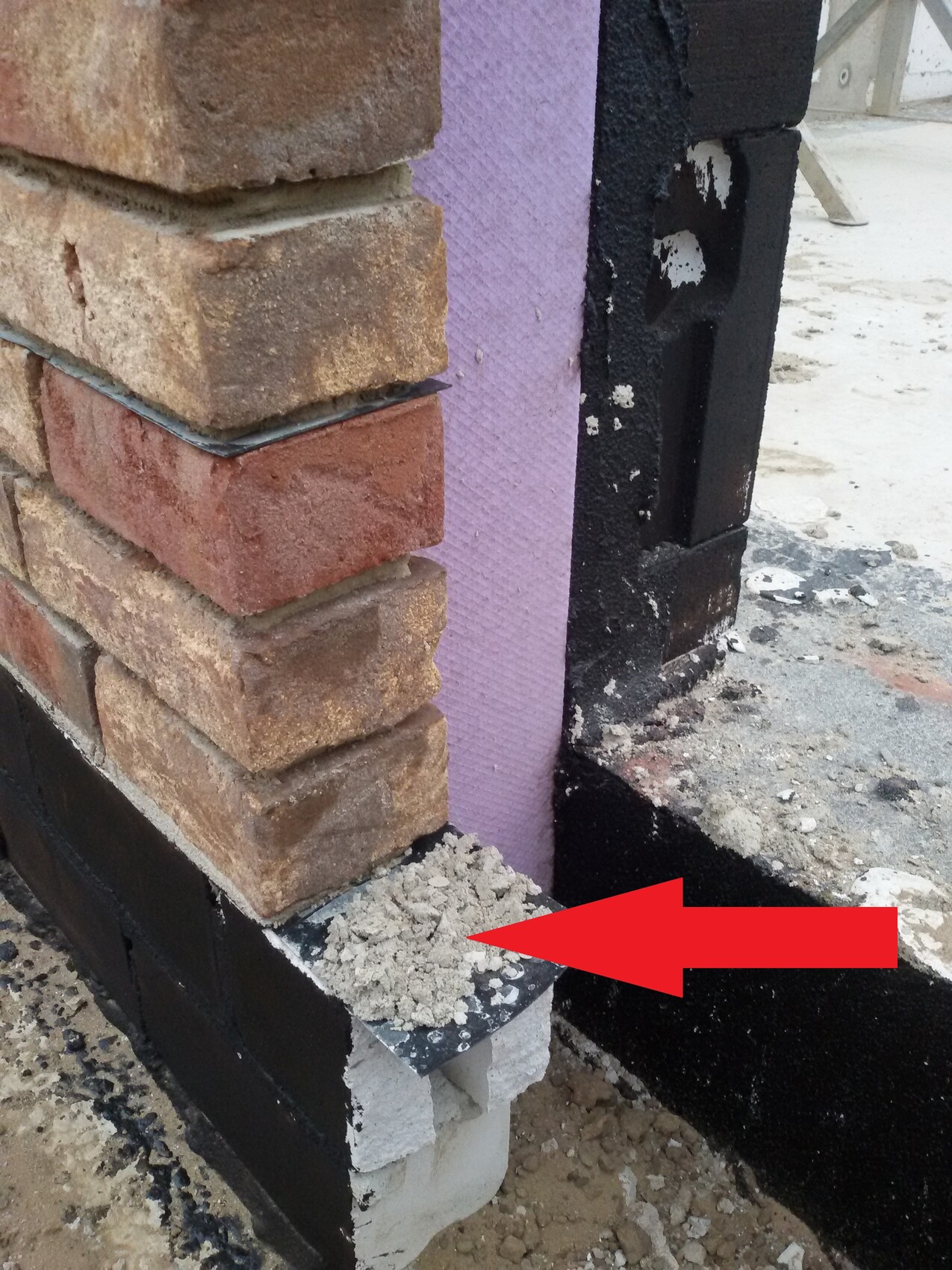 Ecke einer Ziegelwand mit lila Dämmplatten, schwarzer Abdichtung und Kieselbruch am Fundament.