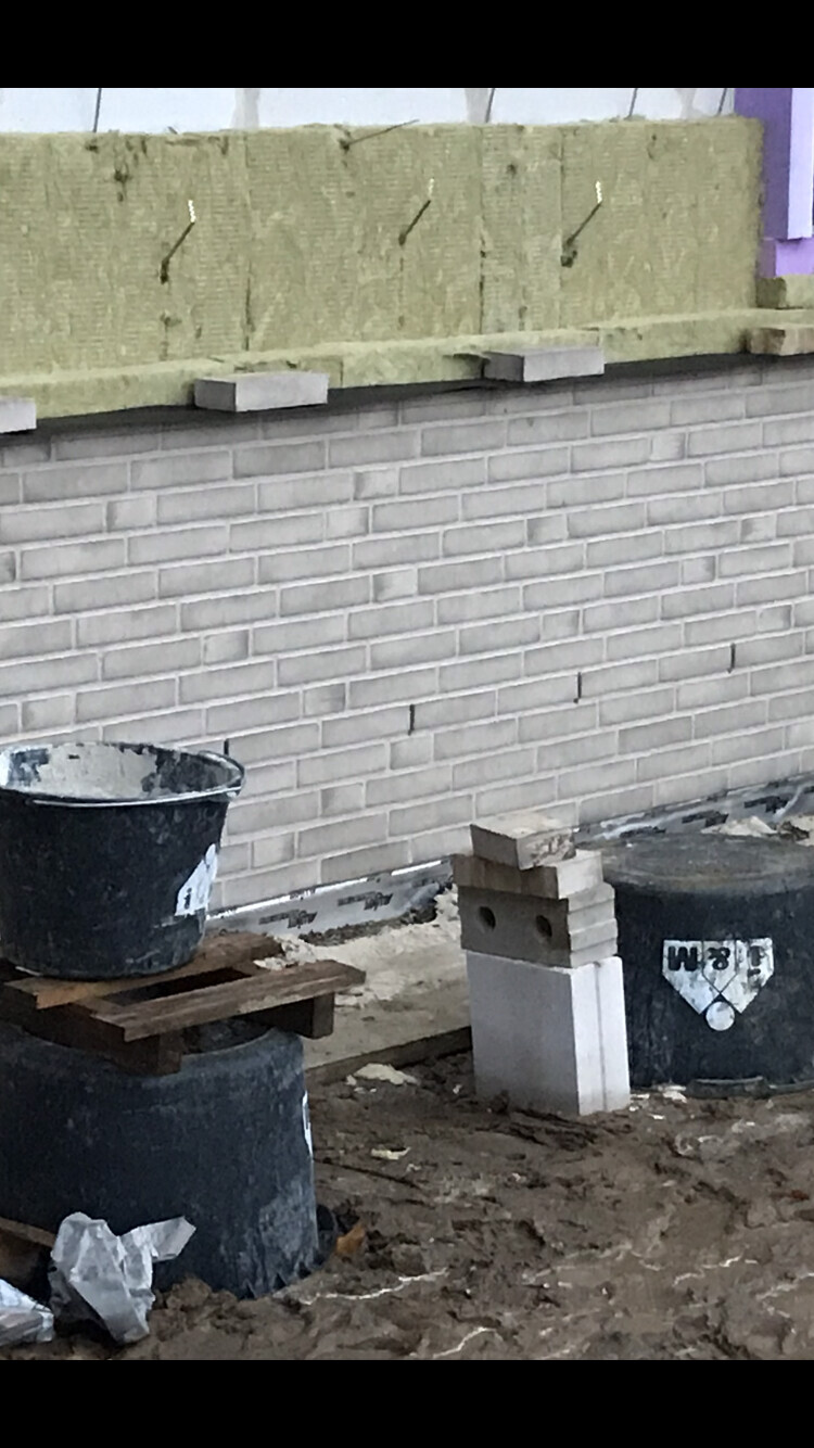 Außenwand mit Dämmplatten, Fundamentsteine und Bauutensilien auf einer Baustelle