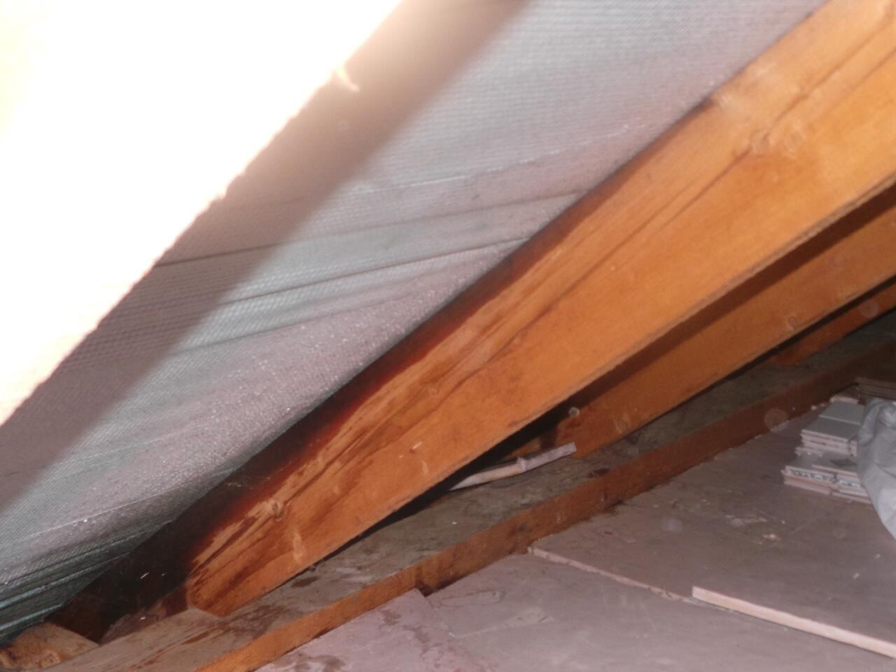 Dachboden mit geneigter Decke, Holzbalken, Dämmmaterial und staubigem Boden; Kartons rechts.
