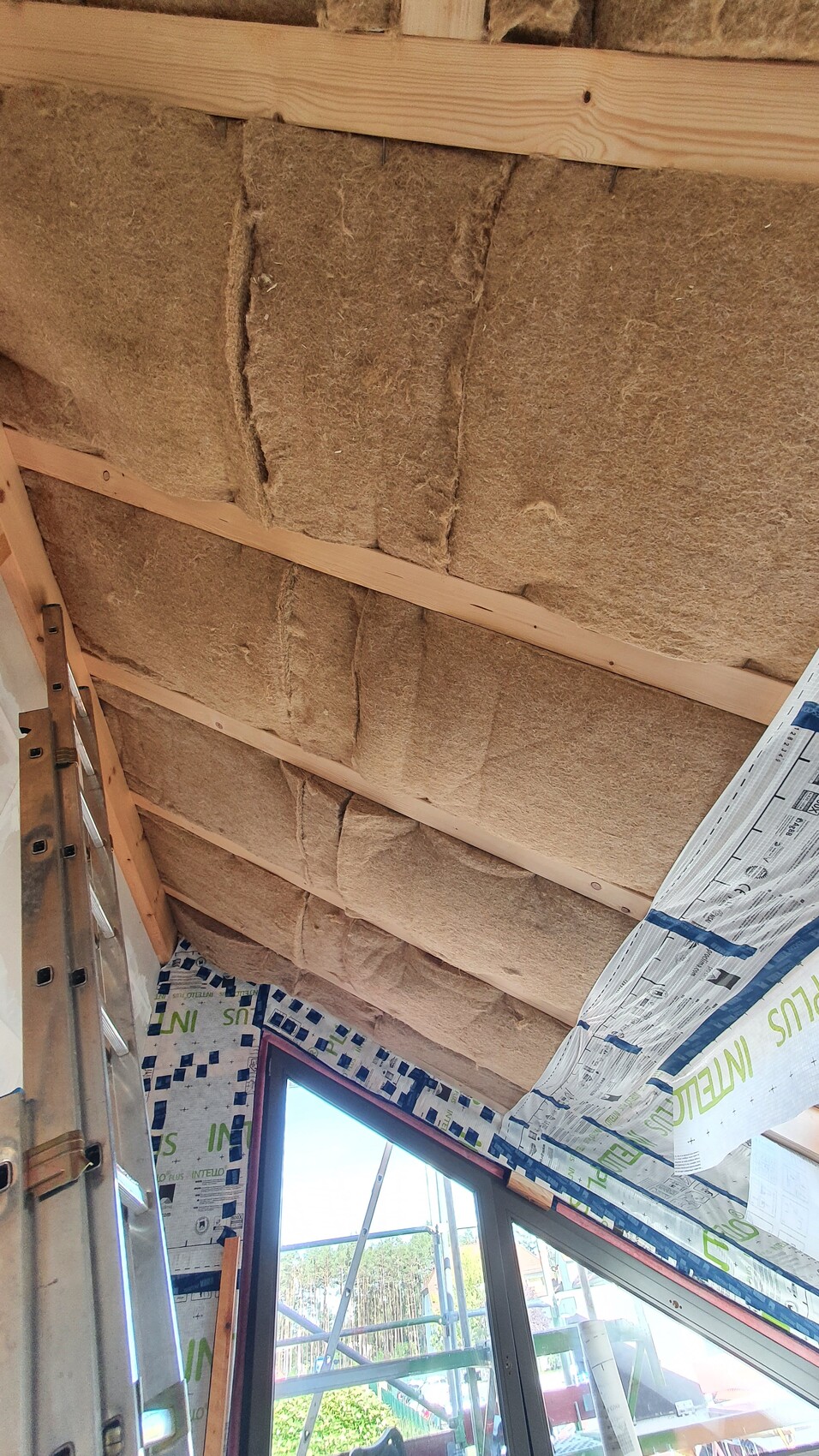 Dachgeschoss-Baustelle: Dämmwolle zwischen Holzbalken, Leiter und Fenster.