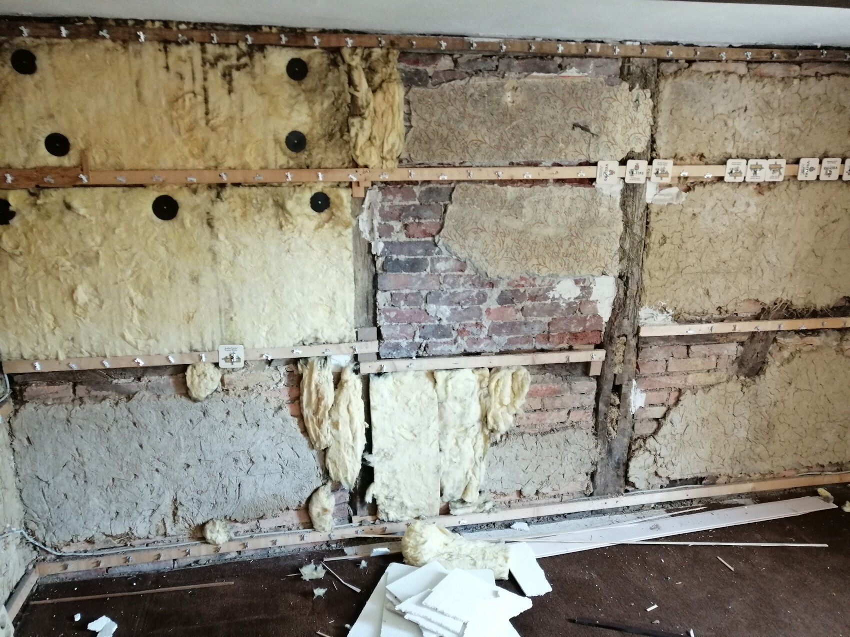Innenwand im Umbau: freigelegte Ziegel, gelbe Dämmung, Holzlatten und Putzreste.