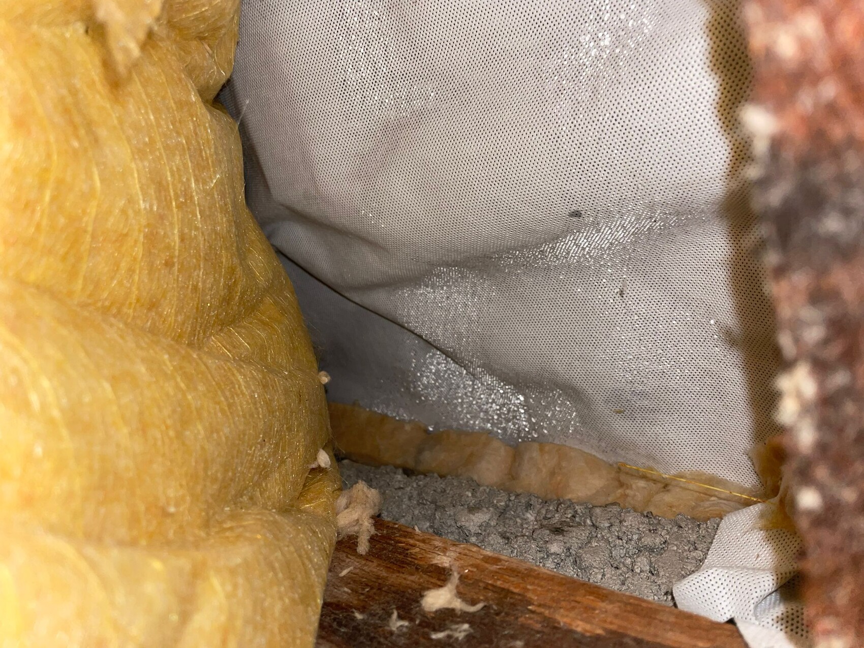 Innenseite einer Wand/Decke mit gelber Glaswolle-Dämmung, graue Dampfbremse und Holzbalken.