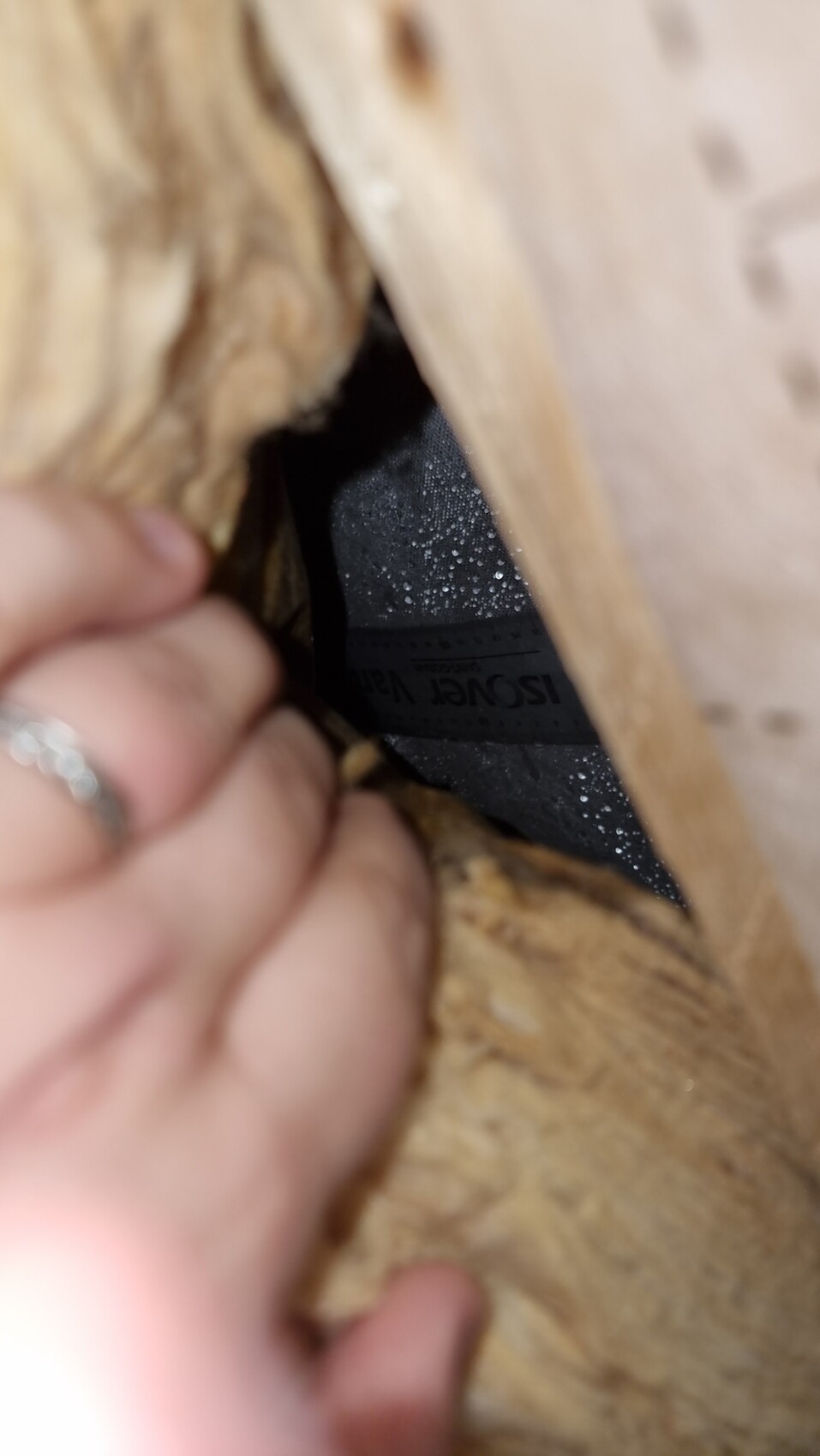 Hand zieht Isover-Isoliermaterial aus einer Wandöffnung hinter Holzrahmen hervor.
