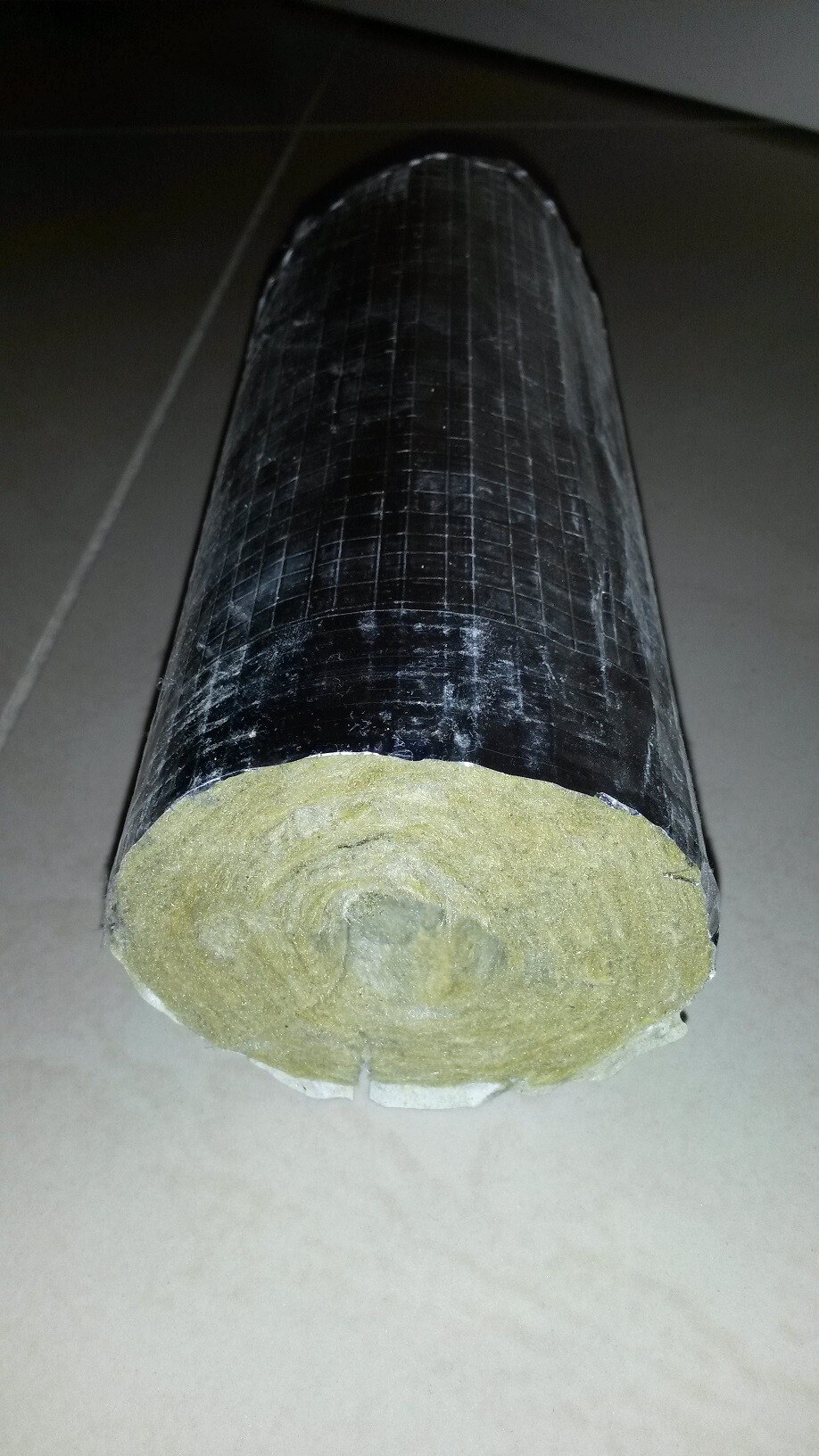 Schwarze Rohrdämmrolle mit gelb-beigem Dämmstoffkern, Endansicht sichtbar.