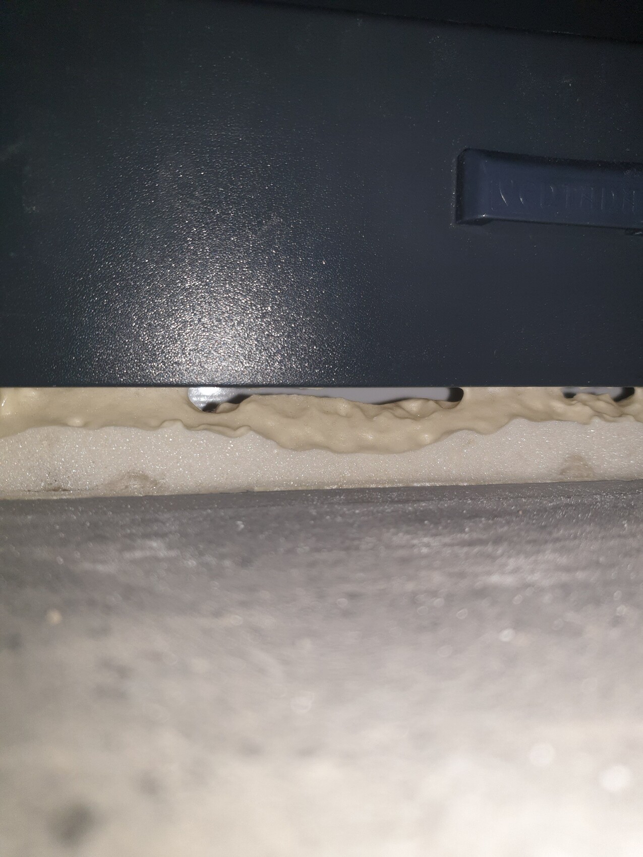 Nahaufnahme eines dunkelblauen Metallgehäuses mit beigem Dichtungs-Schaum an einer Spalte