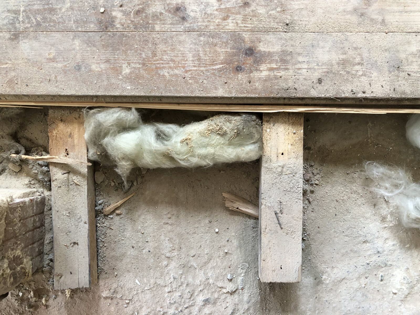 Unterboden mit losem Glaswolle-Dämmstoff zwischen Holzbalken, Staub und Holzreste