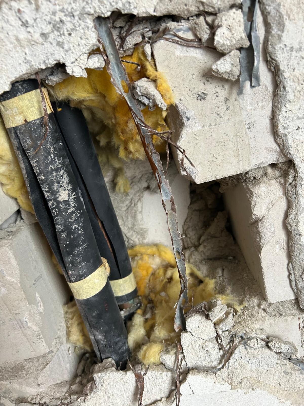 Freigelegte Wand mit schwarzen Rohren, gelber Dämmung und Bruch im Beton