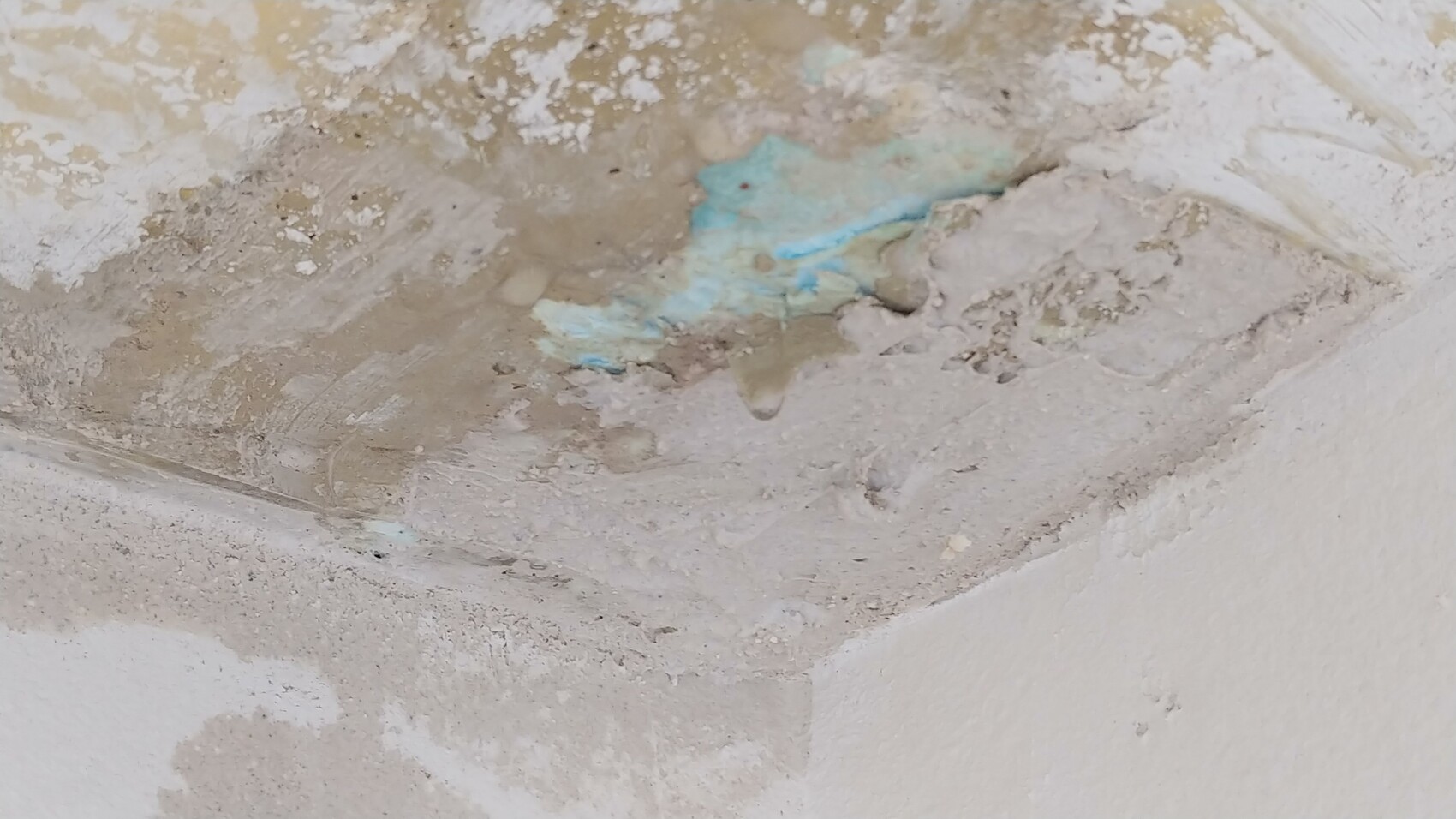 Rohbau-Wand mit abgeplatztem Putz und sichtbarer blauer Dämmung aus Schaumstoff