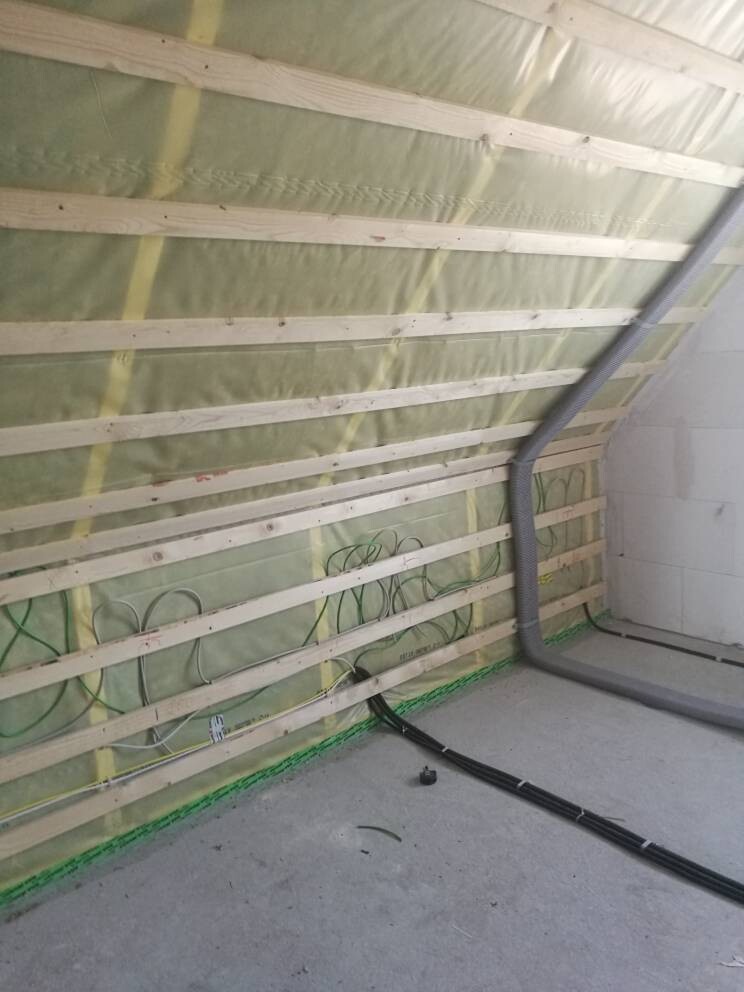 Unbearbeiteter Innenraum: Wand mit Holzlatten, Dämmung, Kabelstrang und flexibler Lüftungsschlauch.