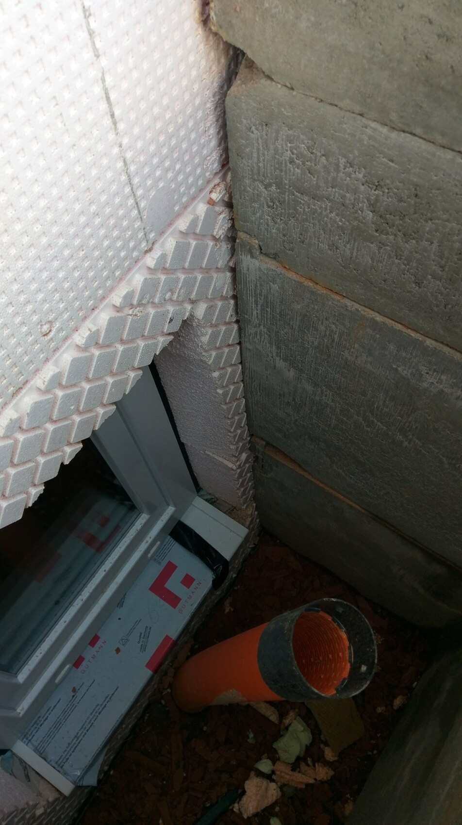 Fensterrahmen, Dämmplatten und rohes Mauerwerk auf Baustelle, orange Abflussrohr sichtbar