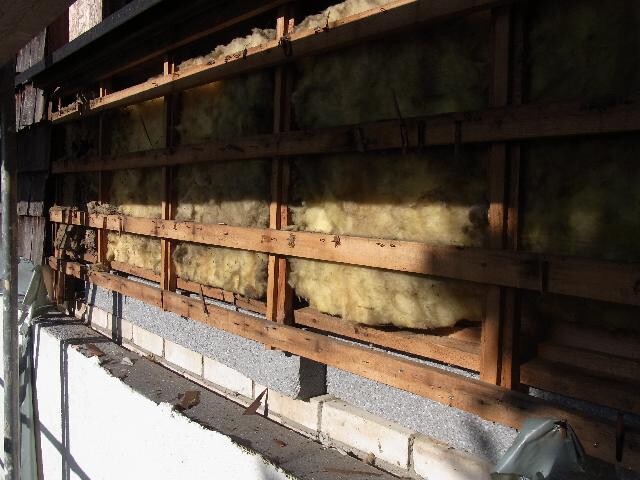 Blick auf Wand mit Holzständerwerk und gelber Dämmung zwischen Balken