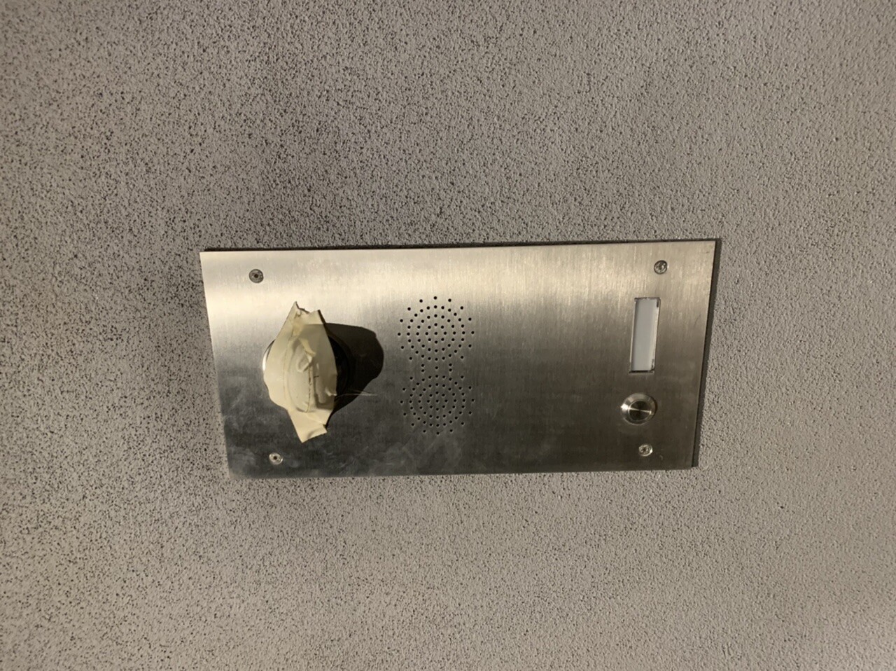 Metallisches Decken-Intercom-Panel mit Lochlautsprecher, klebrig bedeckter Knopf links, Kartenleser rechts.