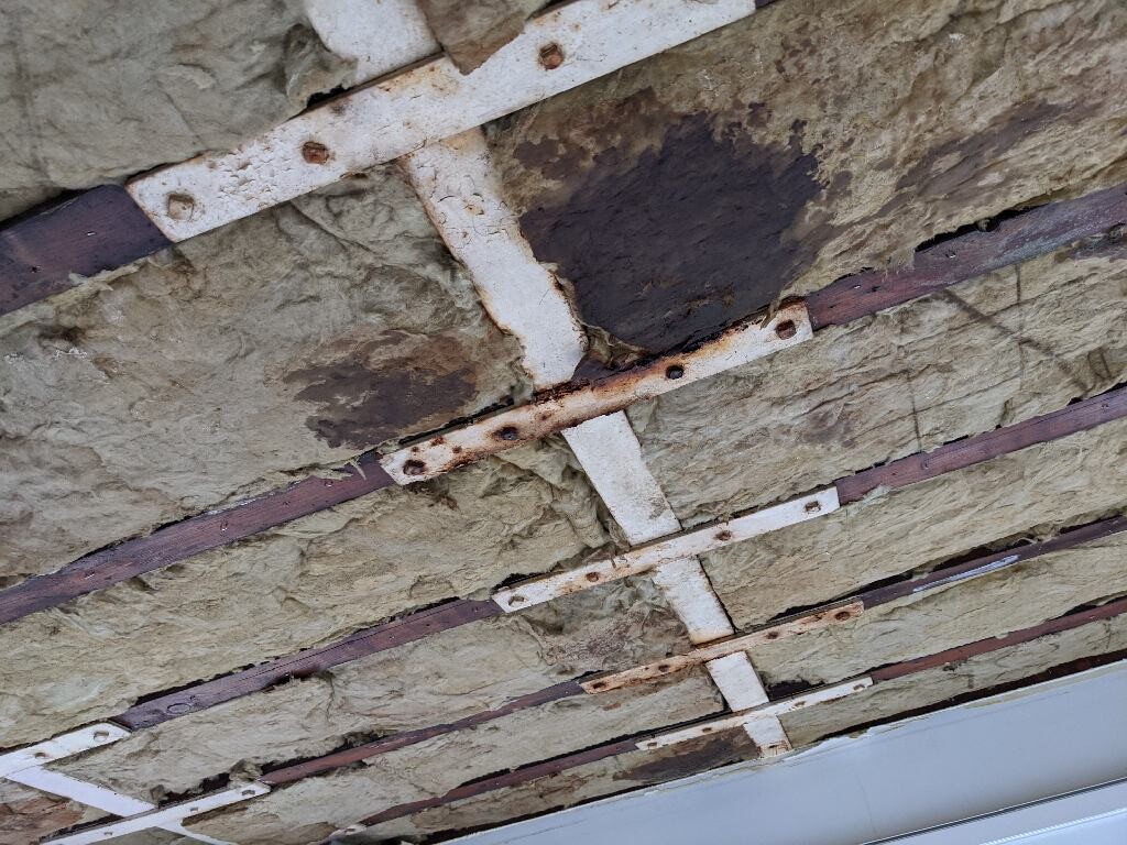 Sichtbare Steinwolle-Dämmung zwischen rostigen Metallträgern an der Decke.
