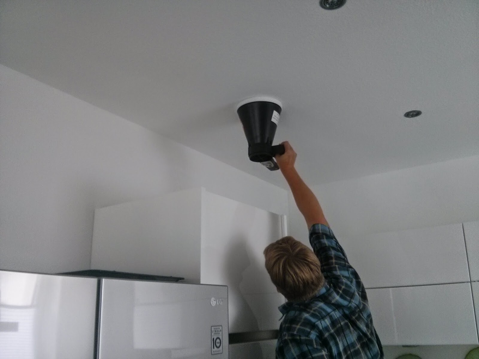 Mann montiert Deckenlampe in moderner Küche, Kühlschrank sichtbar