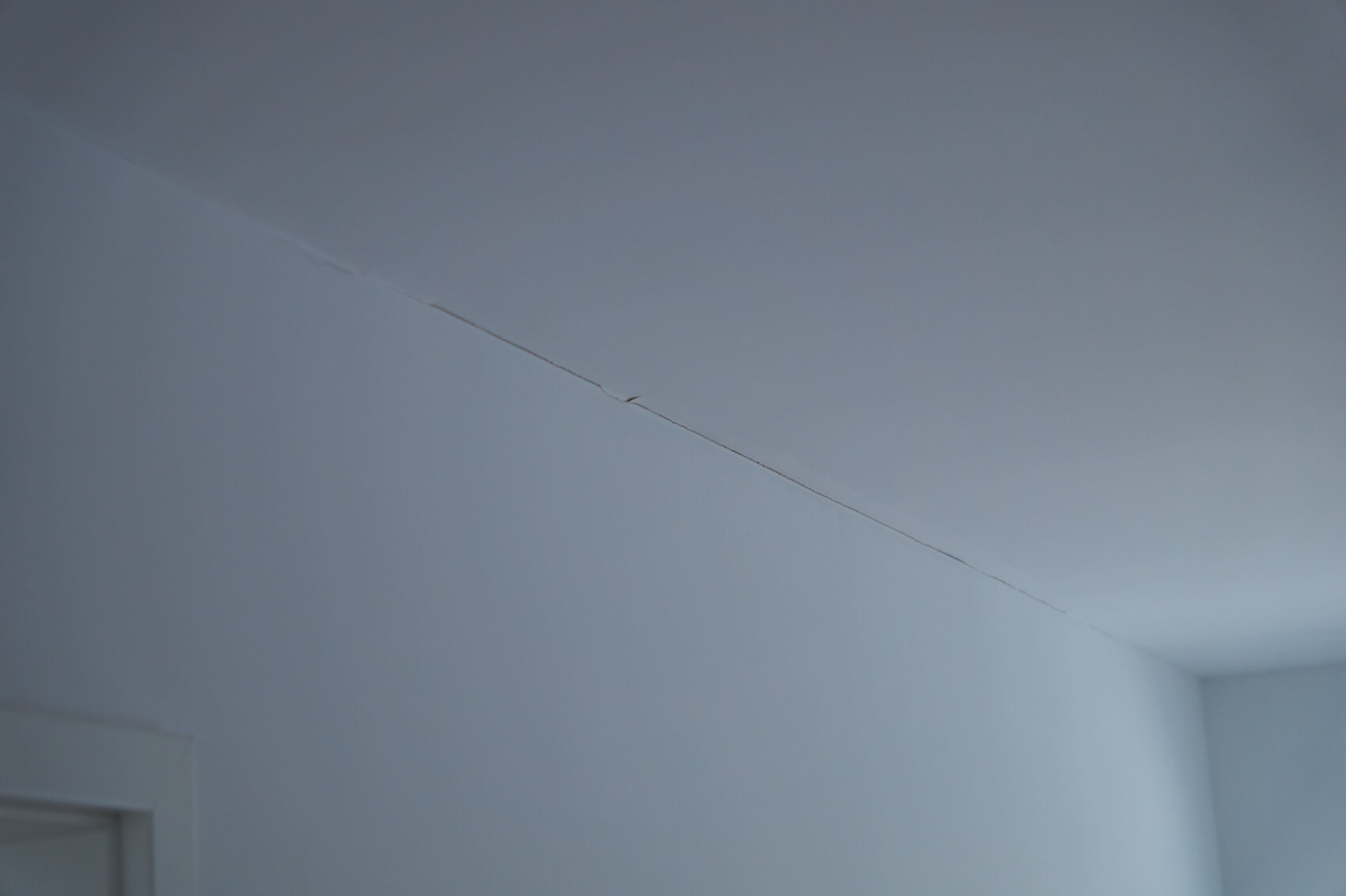 Diagonaler Riss an der Decke eines hellblauen Zimmers; Ecke unten links sichtbar.