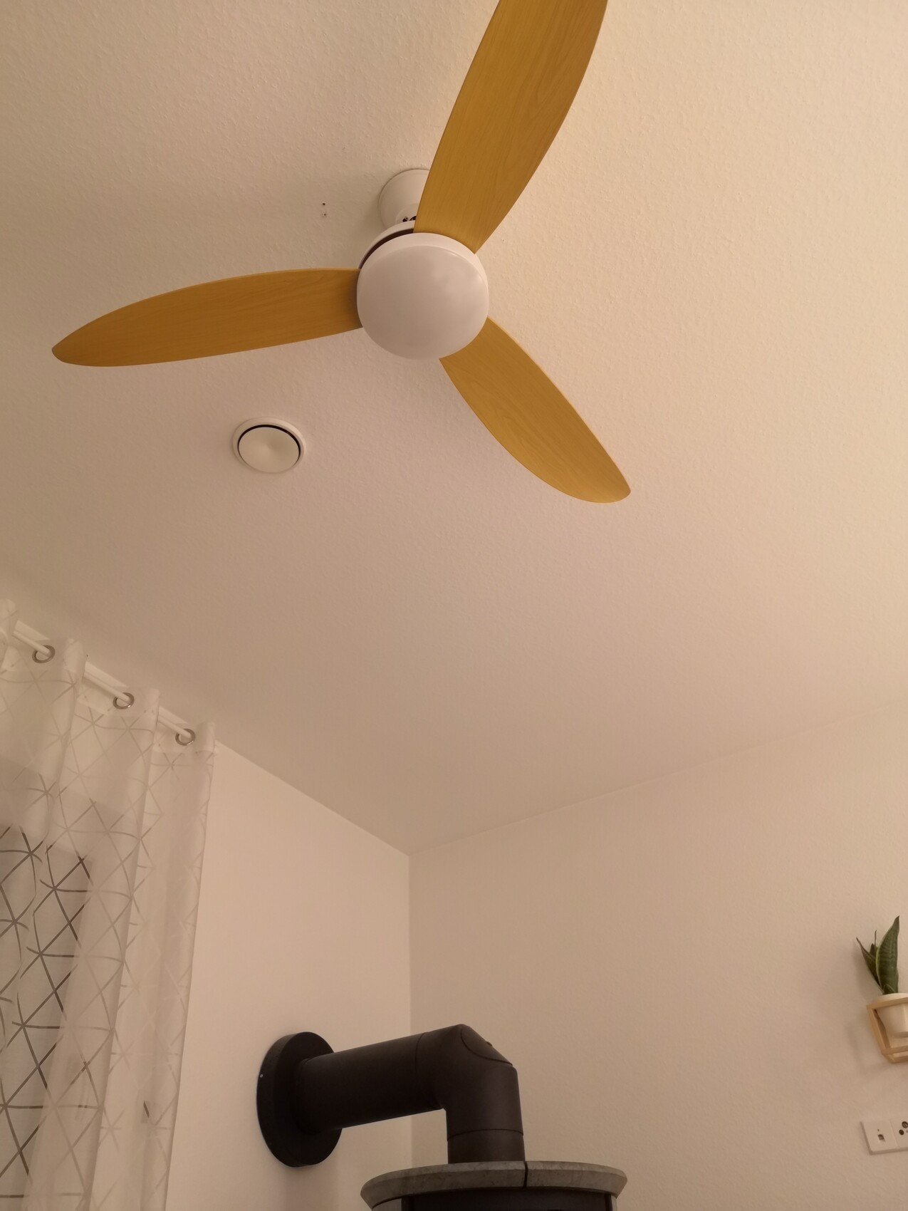 Deckenventilator mit drei Holzflügeln an weißer Decke; Badezimmer mit Dusche sichtbar.