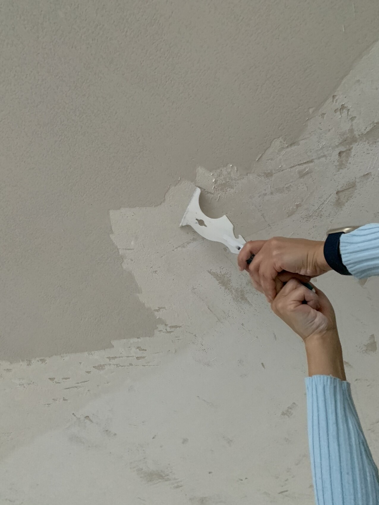 Person glättet feinen Putz an einer Decke mit Spachtel.