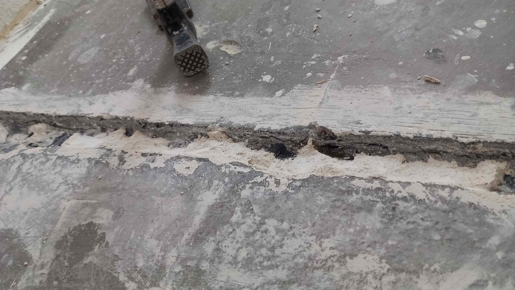 Bruchkante eines Beton-Estrichbodens mit Staub, Riss und kleinem Werkzeug im Randbereich