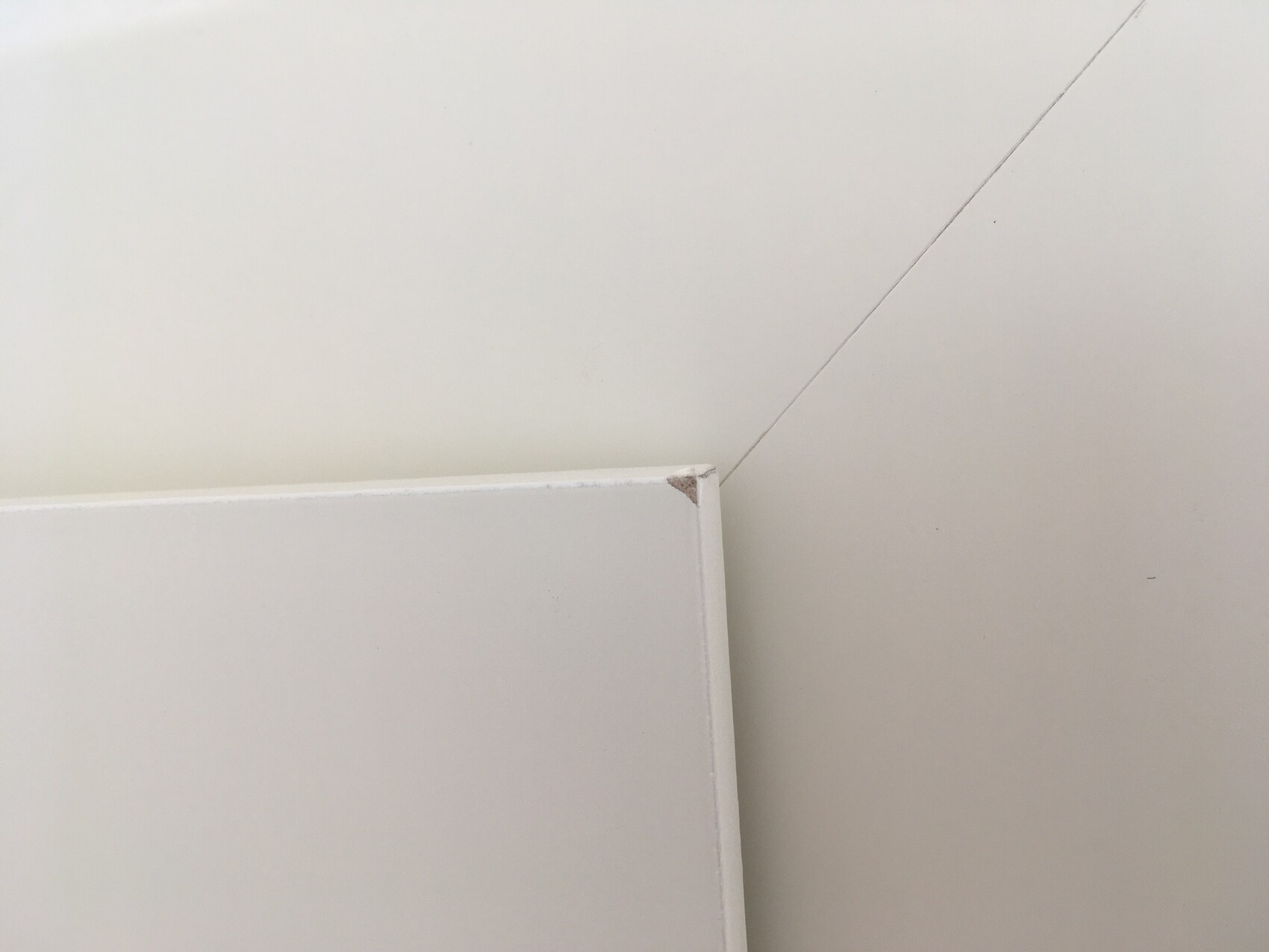 Weiße Möbelkante mit kleinem Eckenabrieb, vor heller Wand mit diagonaler Fuge.