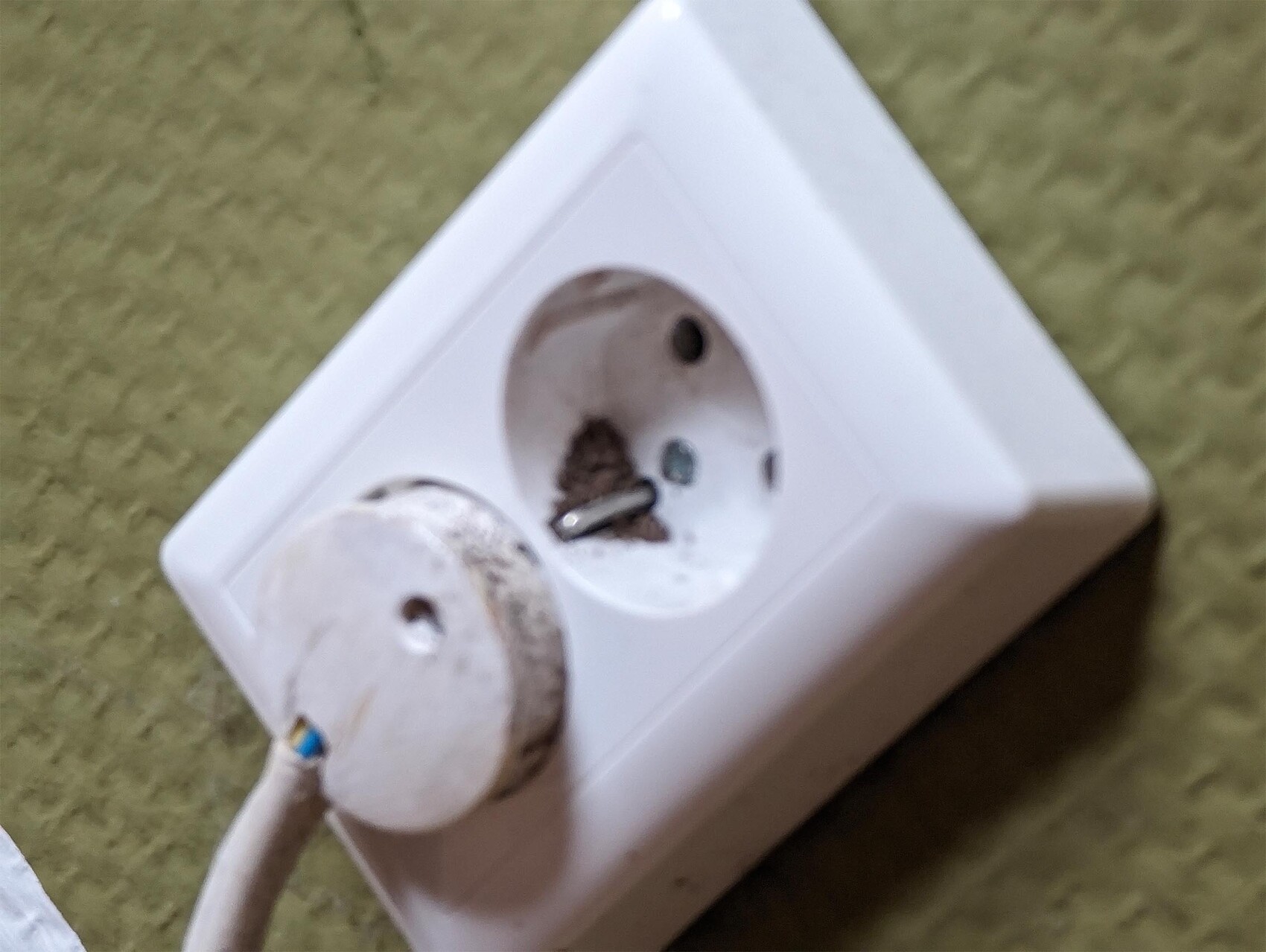 Weißes Doppel-Steckdosenpanel mit verschmutzten Kontakten; Staub und ein losem Teil daneben.