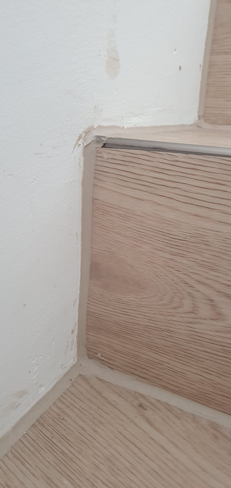 Innenwand-Ecke: weiße Wand, Holzoptik-Boden, Metall-Übergangsleiste, Ecke leicht beschädigt