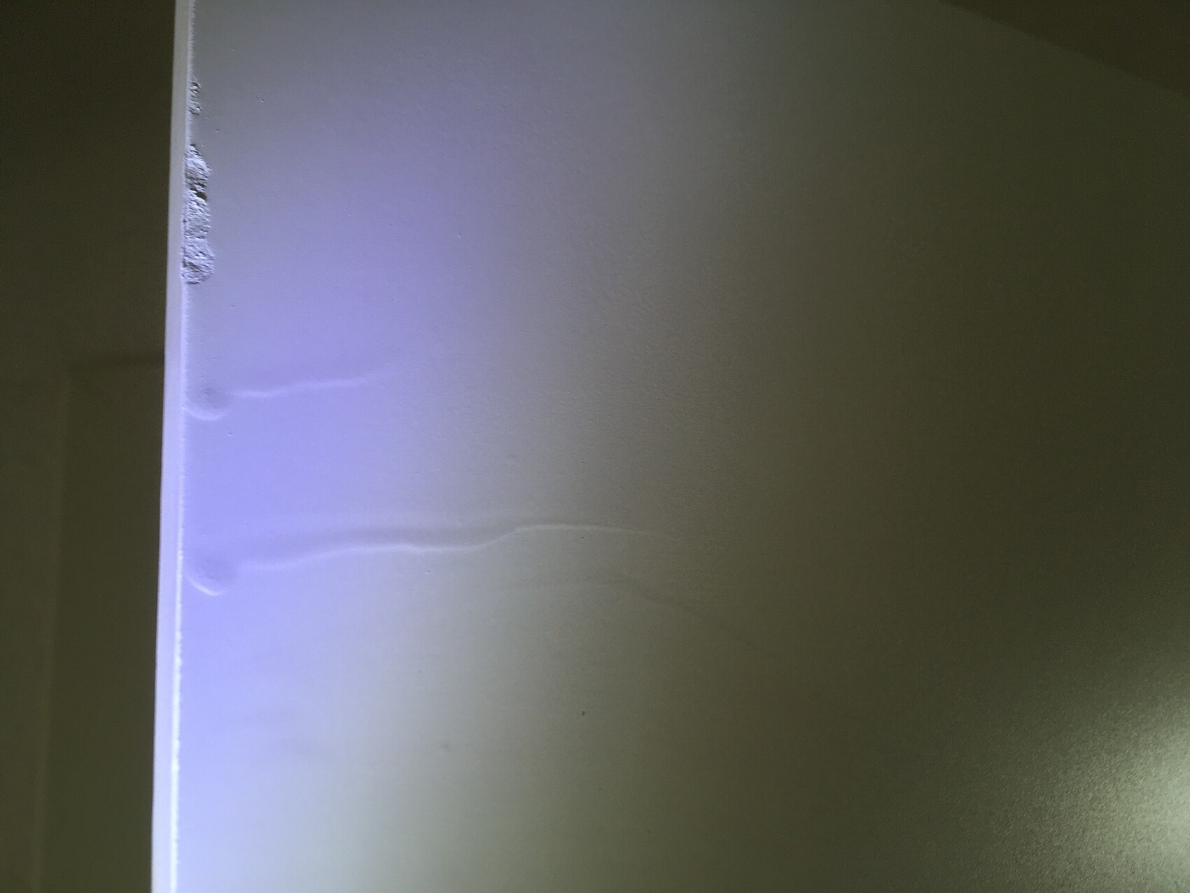 Nahaufnahme einer glatten Wand mit linker Kante und Unregelmäßigkeiten, blau-violette Beleuchtung.