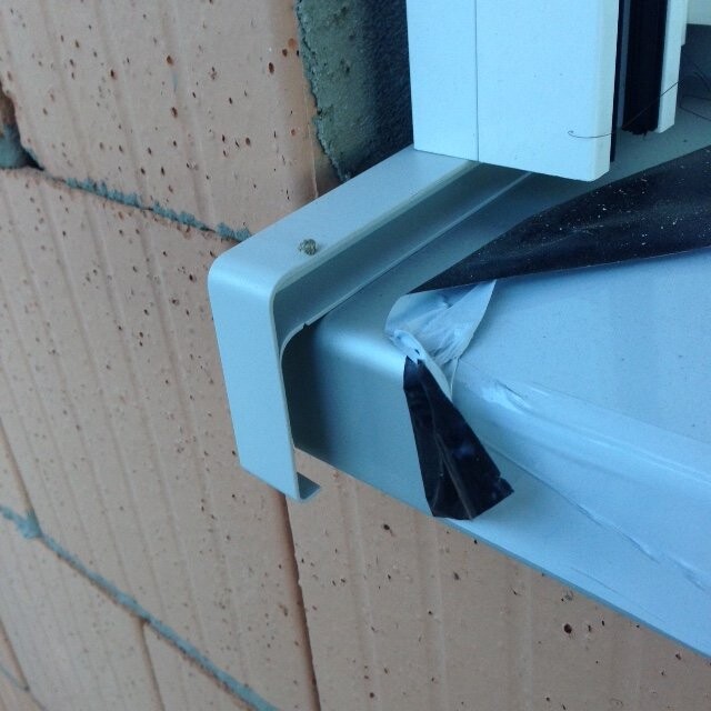 Nahaufnahme eines Metall-Fensterrahmens mit Klebeband an einer Backsteinwand.