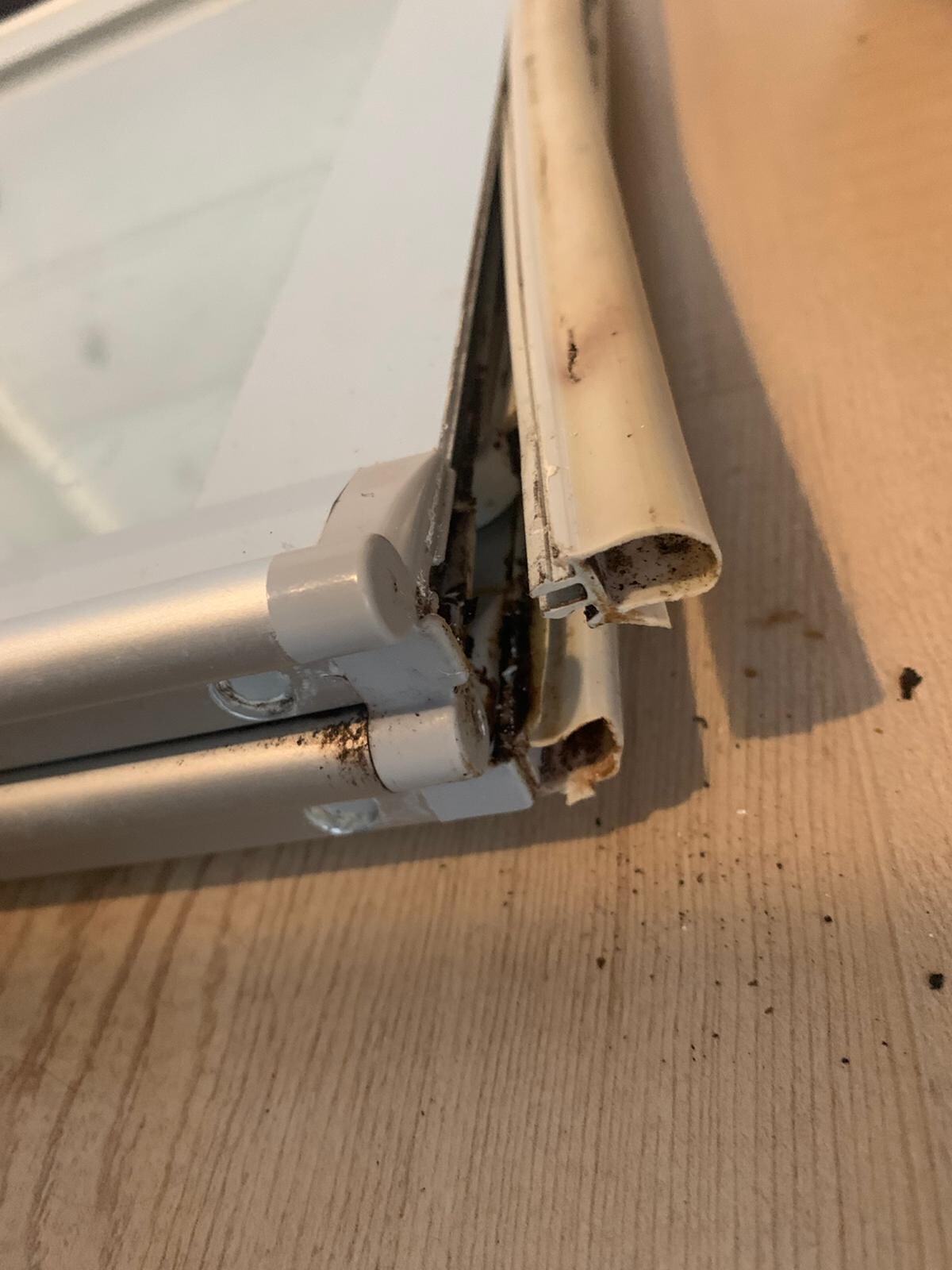 Nahaufnahme eines beschädigten weißen Fensterrahmens mit losem Dichtungsprofil und Rost am unteren Rand.