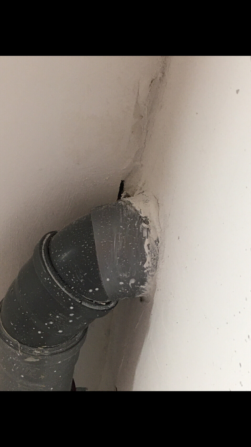 Grauer PVC-Bogen in der Wand, umgeben von bröckelndem Putz und Staub.
