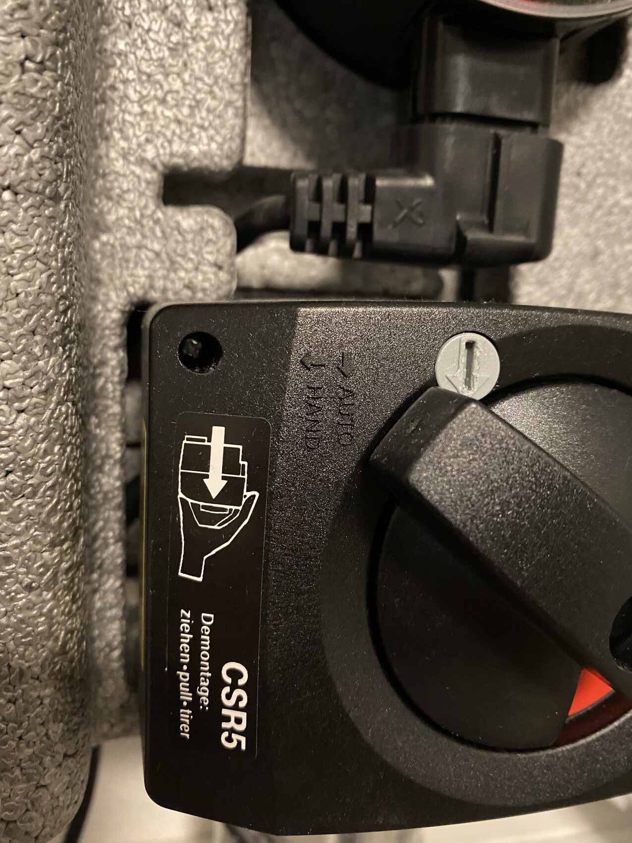 Nahaufnahme eines schwarzen Kunststoff-Adapters mit Demontage-Anleitung und einer ziehenden Hand.