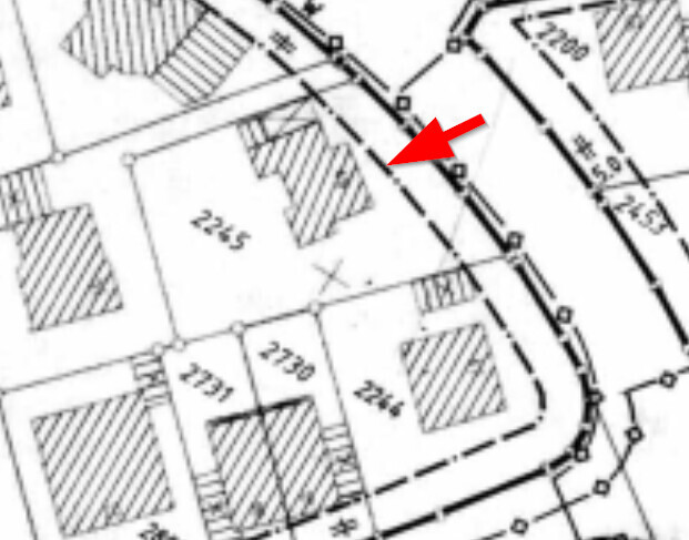 Lageplan eines Baugrundstücks; roter Pfeil markiert Parzelle neben einer kurvigen Straße.