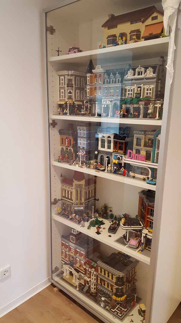 Glasvitrine voller LEGO-Stadtgebäude, Minifiguren und Fahrzeugen auf mehreren Regalen.