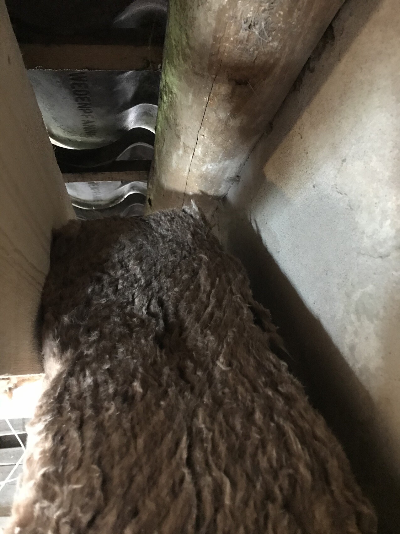 Große braune, faserige Dämmmasse liegt zwischen Holzbalken und Wand auf dem Dachboden.