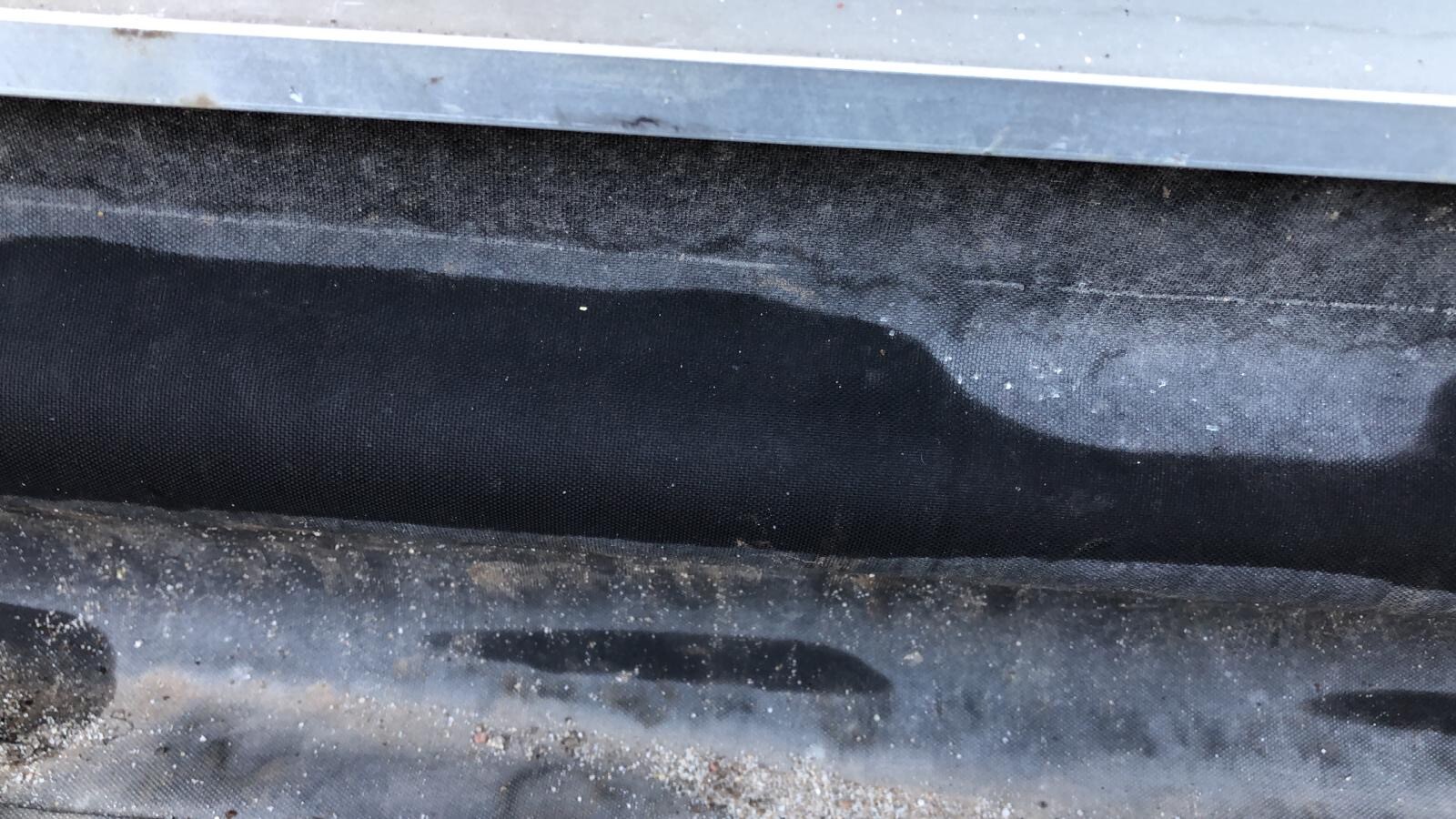 Schwarze Dichtungsbahn aus Baufolie am Fundamentrand mit Staub und Schmutz