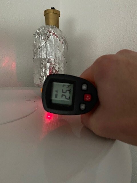 Hand hält Infrarot-Thermometer; zeigt 25,4°C an einer Alufolie-umwickelten Flasche
