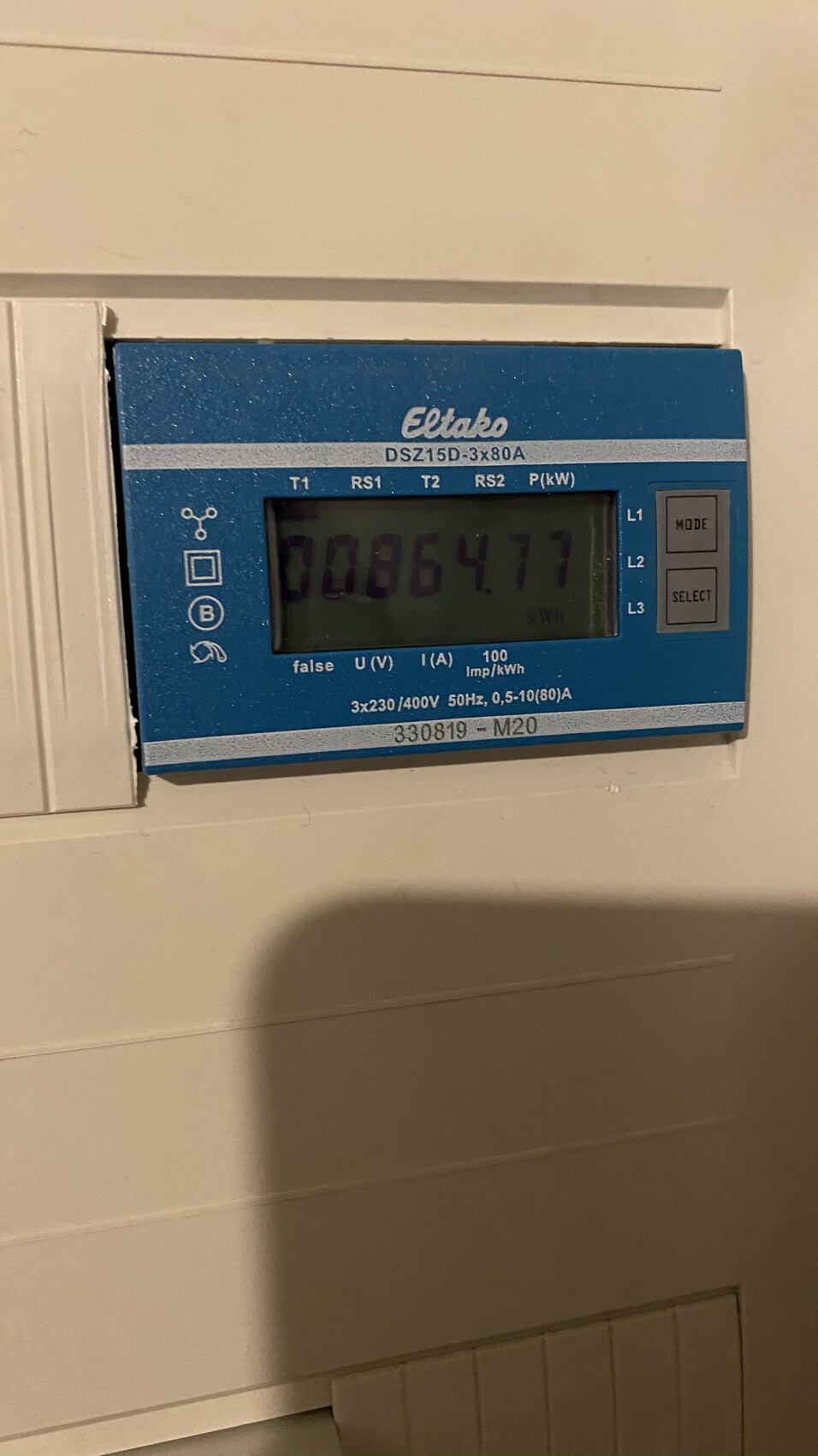 Blauer digitaler Stromzähler an der Wand mit Display und zwei Knöpfen rechts.